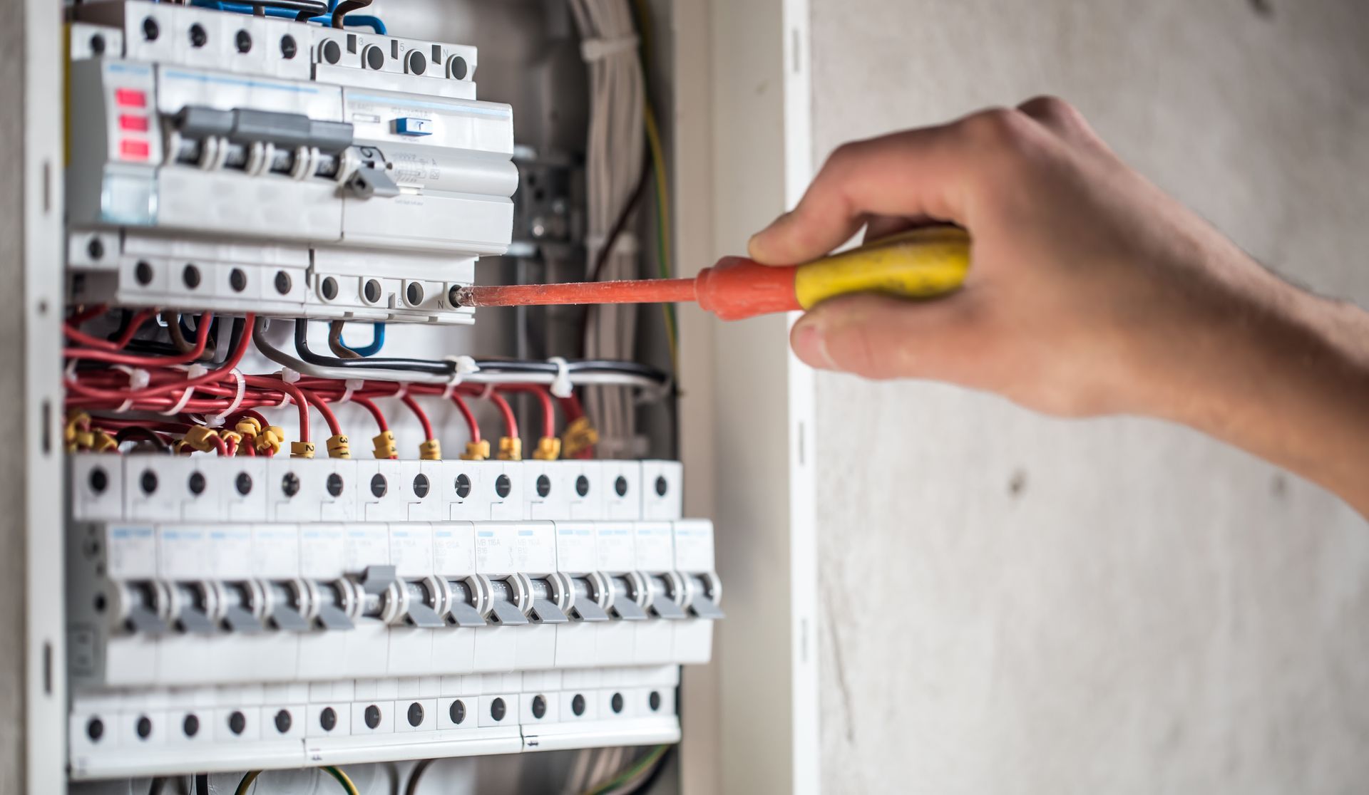 A person is working on an electrical box with a screwdriver.