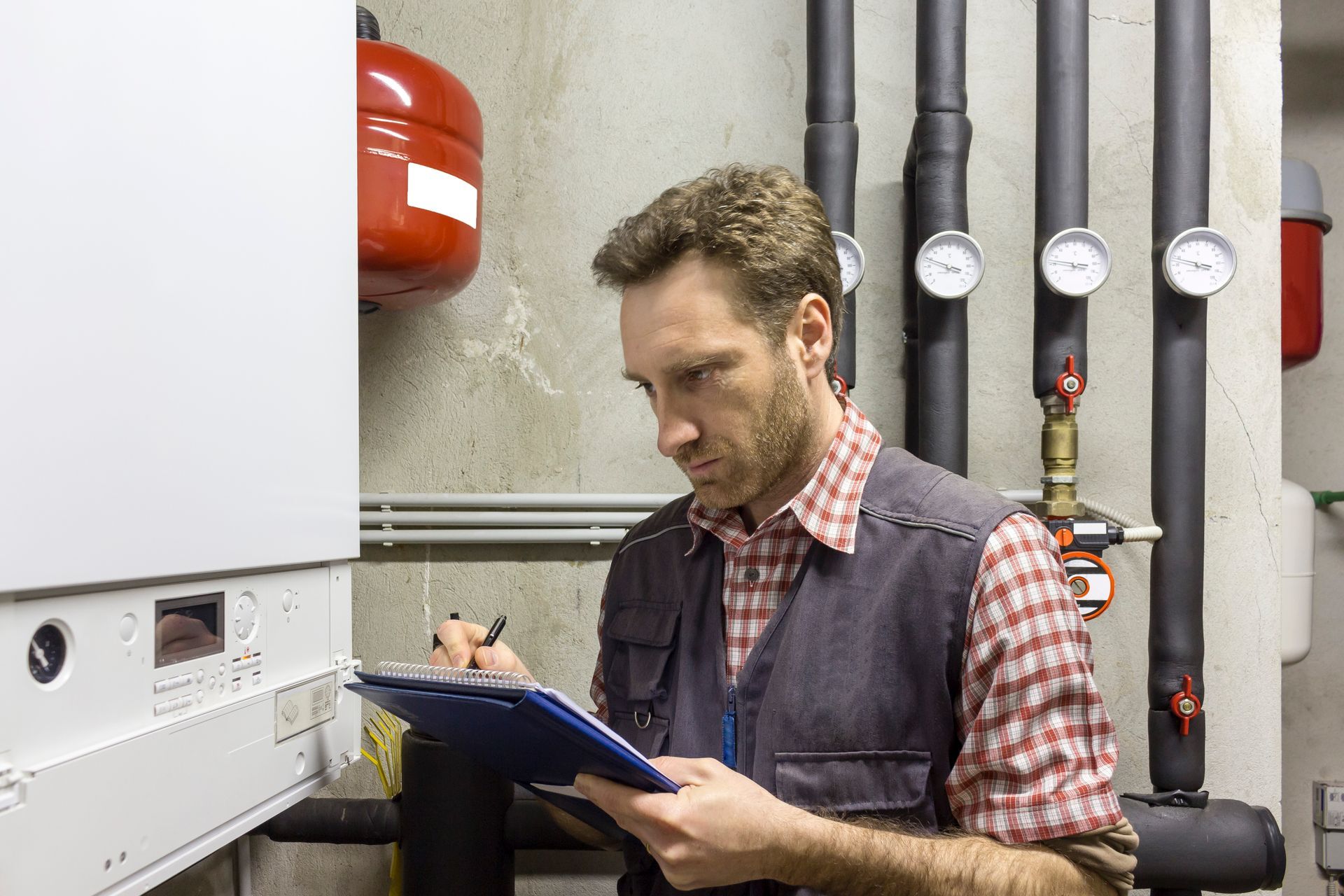 A man is looking at a clipboard in a boiler room.