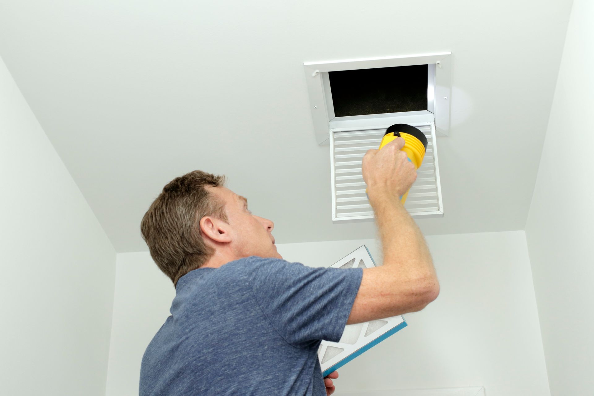 A man is cleaning a vent on the ceiling with a yellow sponge.