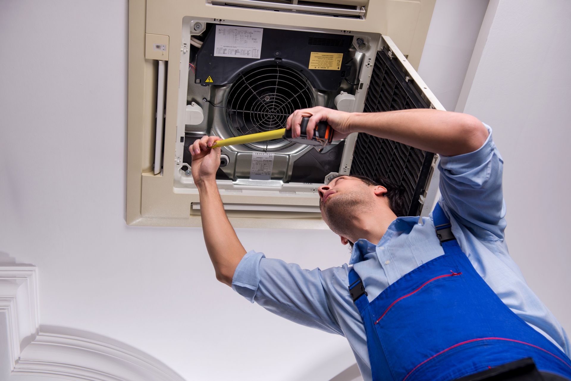 A man is working on an air conditioner with a tape measure.