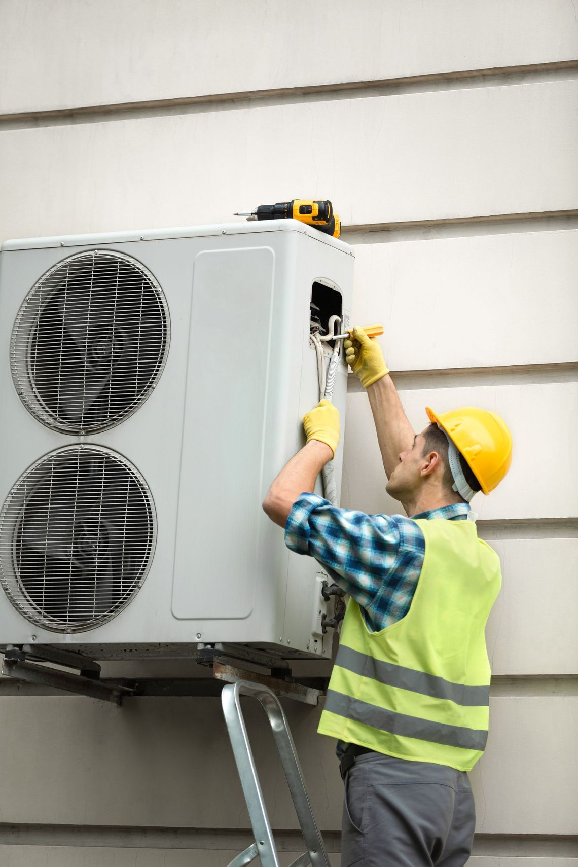 A man is installing an air conditioner on the side of a building.