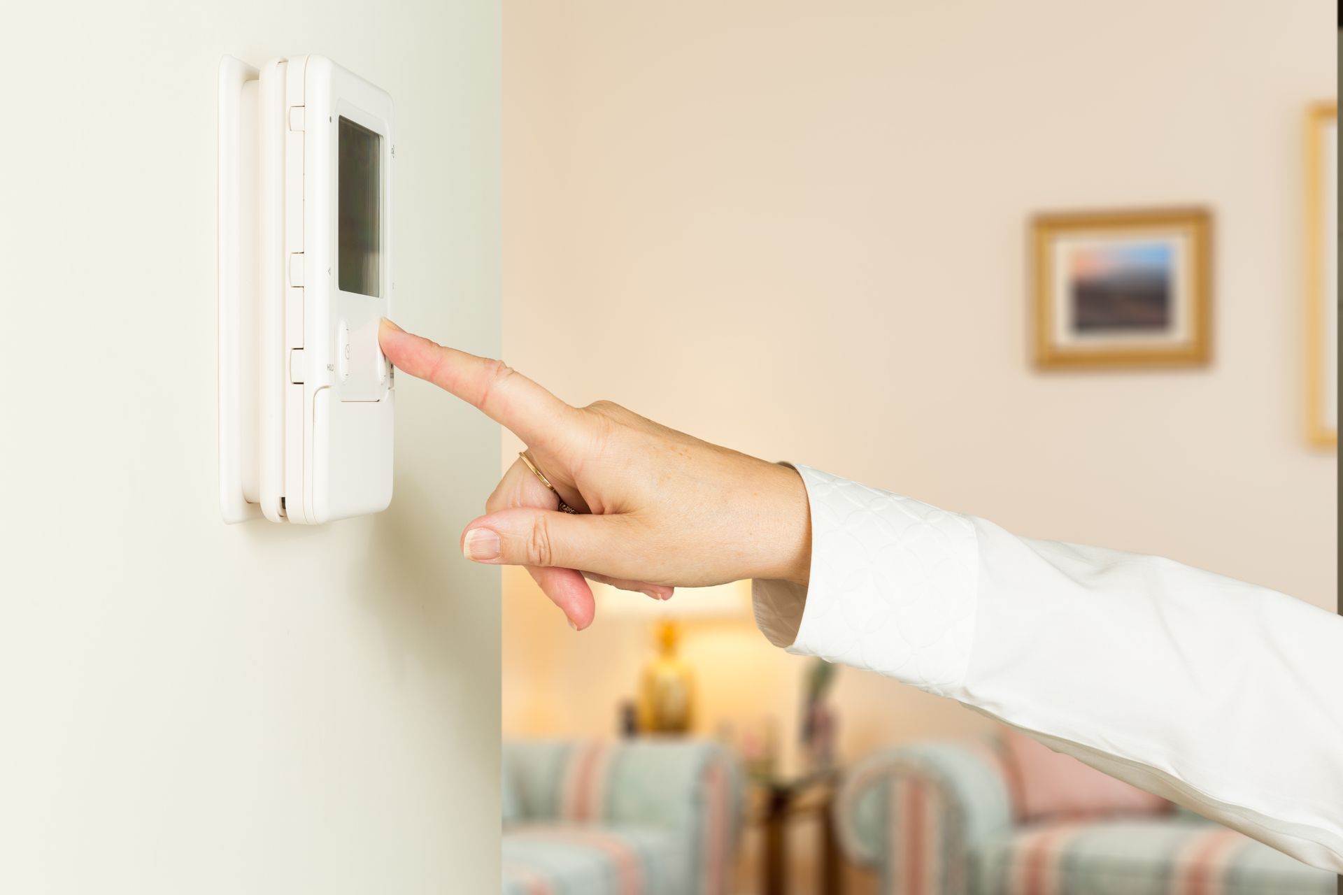 A person is pressing a button on a thermostat in a living room.