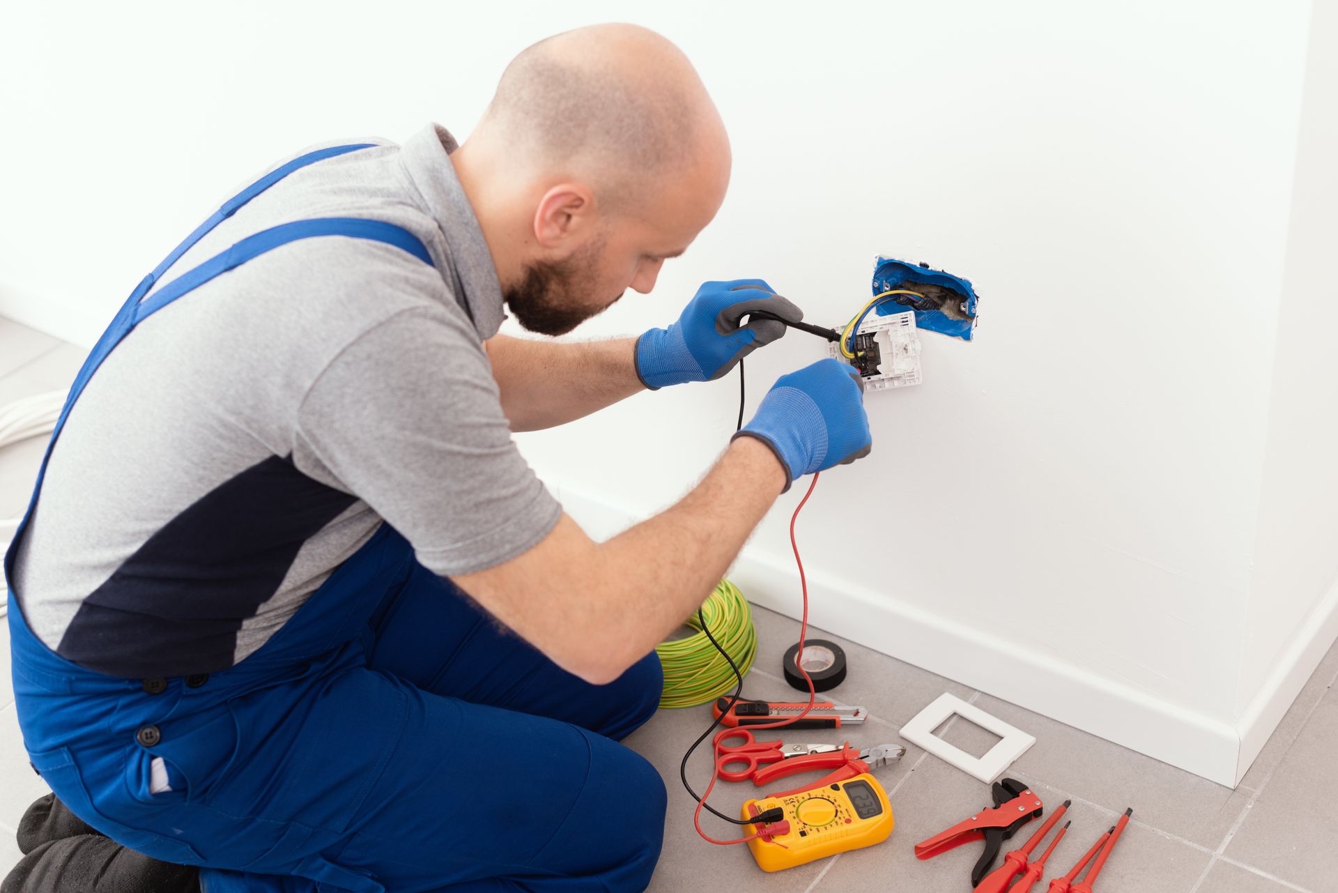 A man is kneeling on the floor working on an electrical outlet.