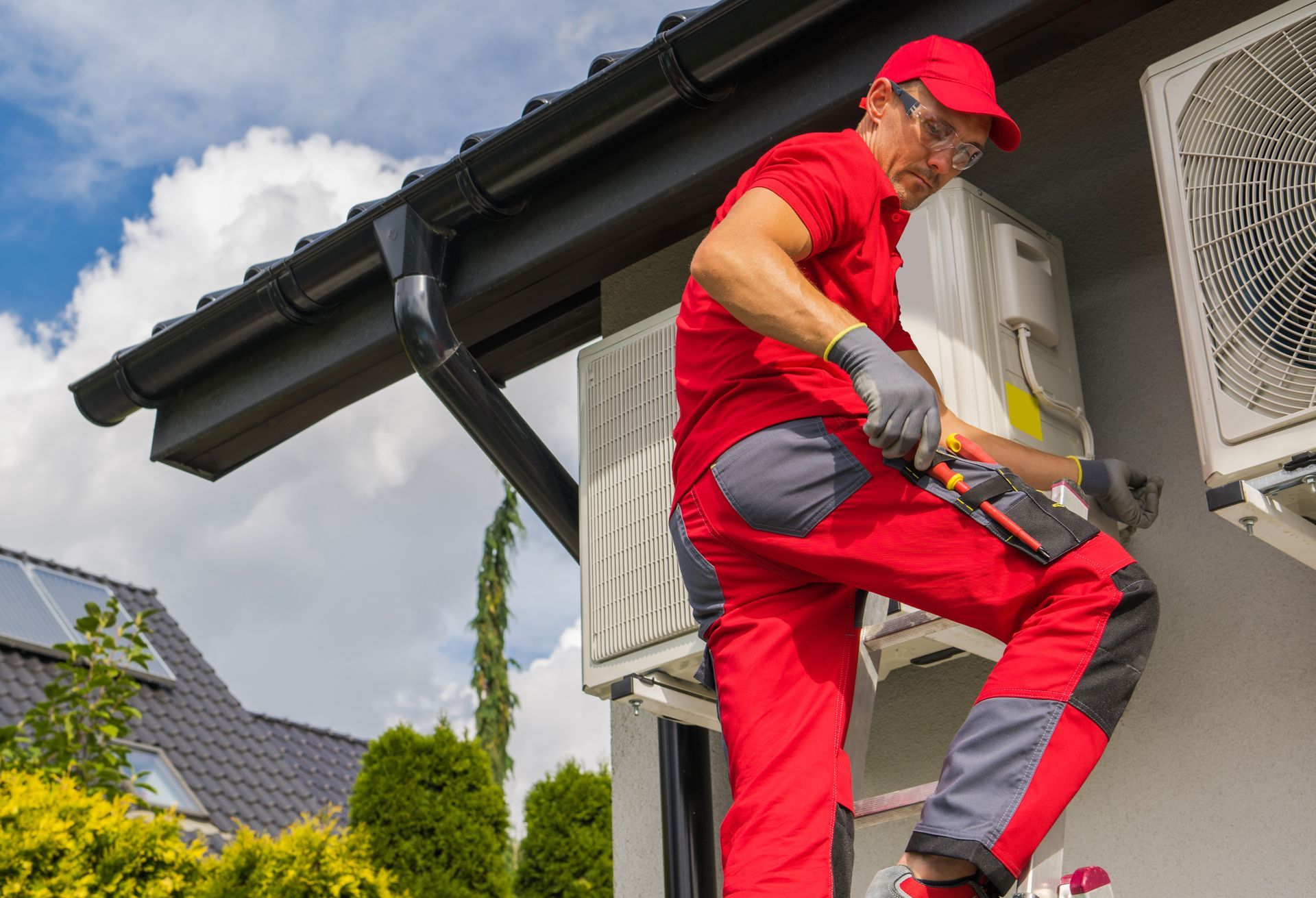 A man is working on an air conditioner on the side of a house.