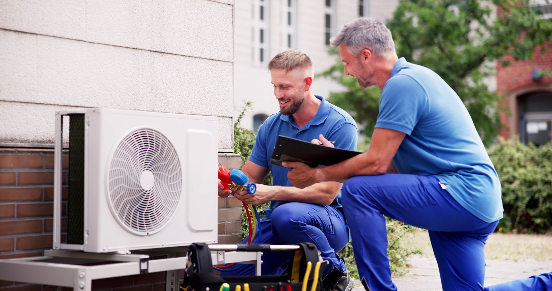 Two men are working on an air conditioner outside of a building.