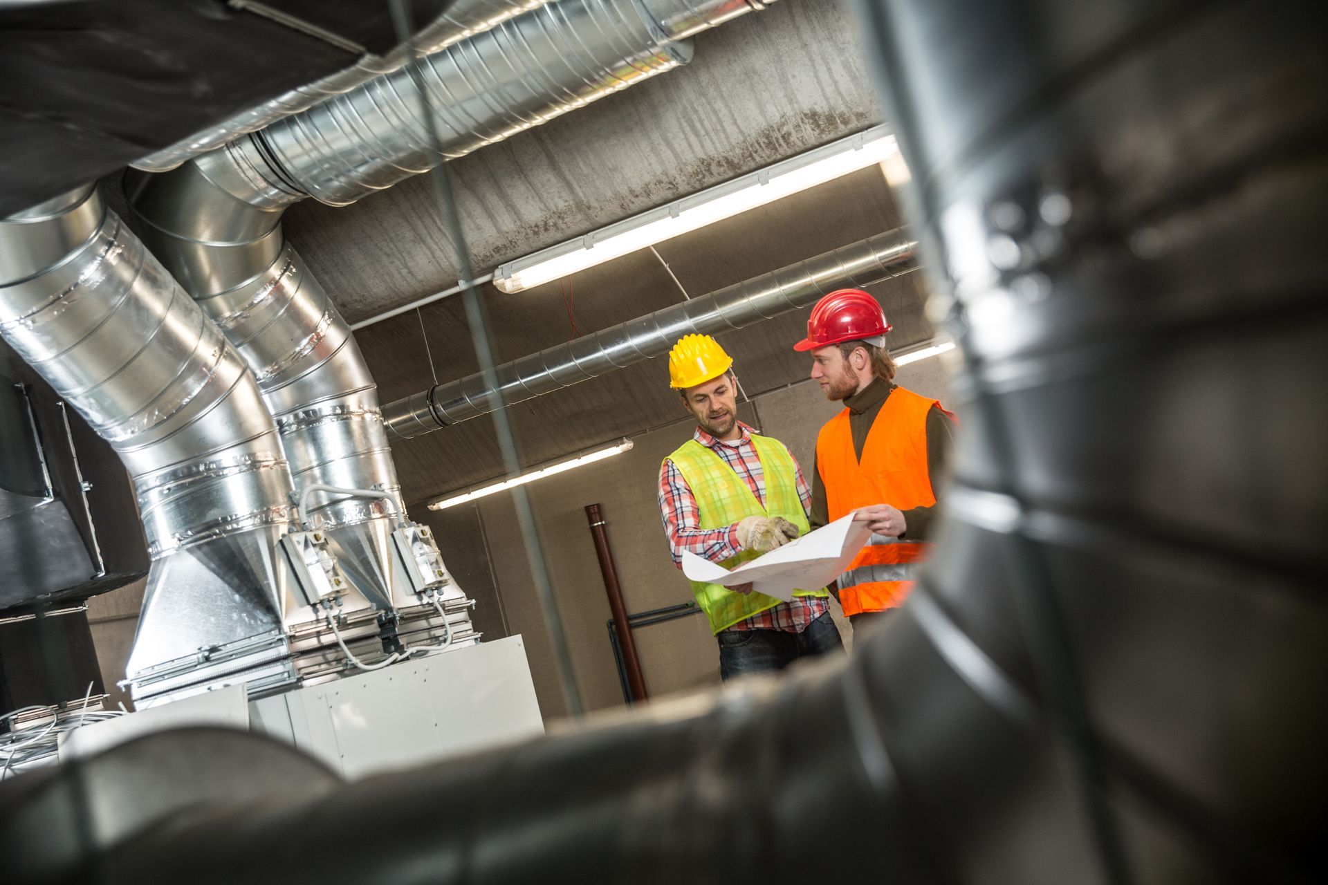 Two construction workers are looking at a blueprint in a factory.