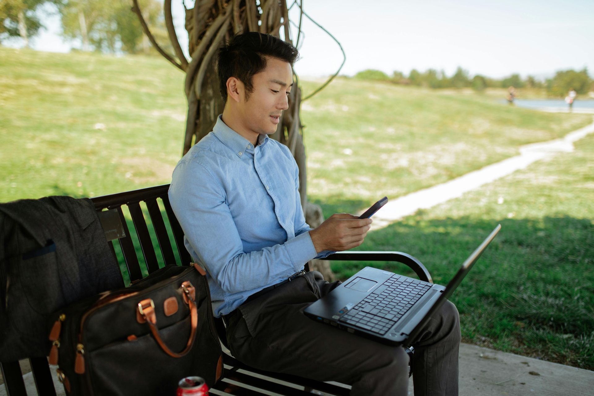 A man is sitting on a park bench with a laptop and cell phone.