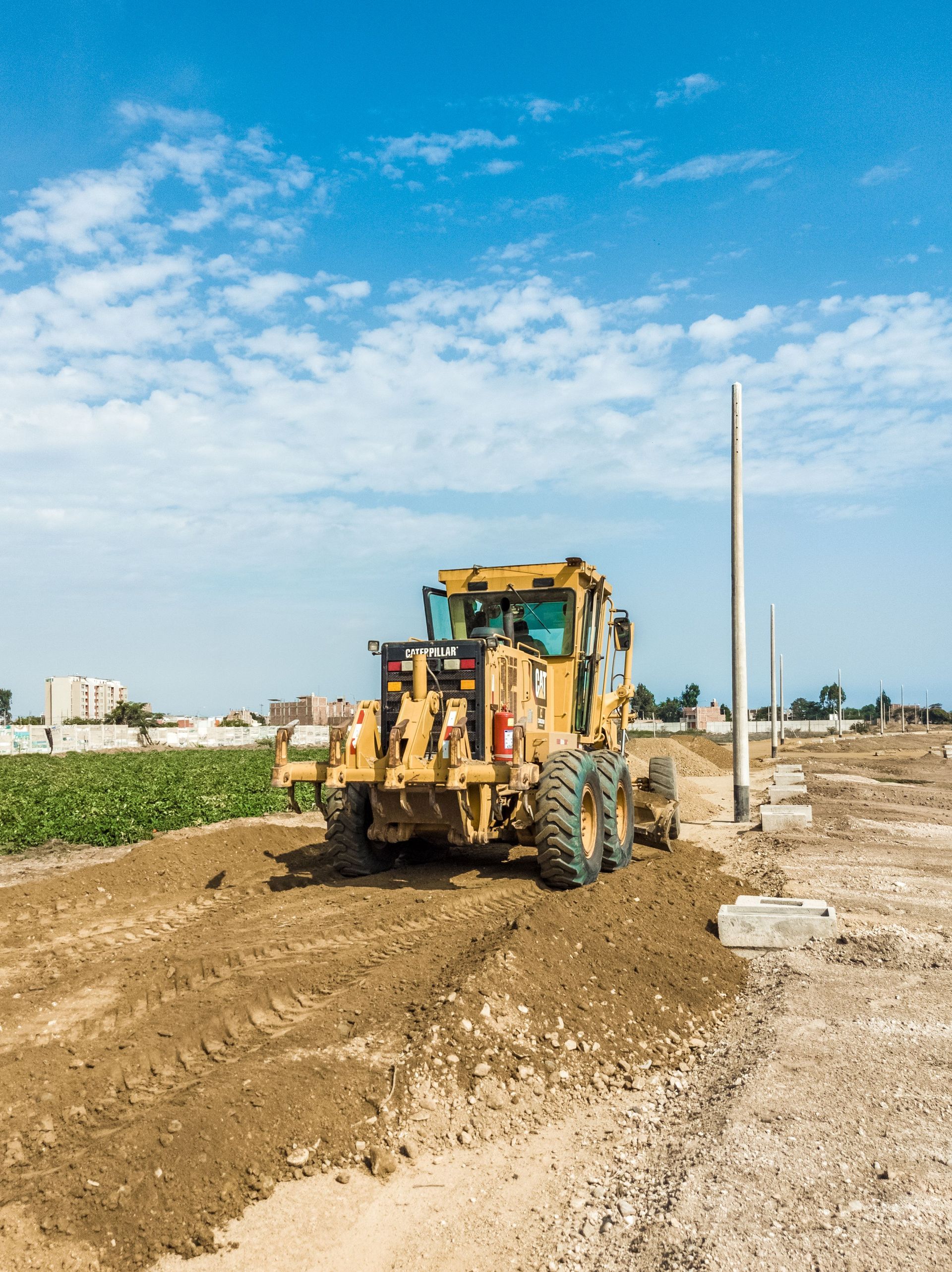 Yellow backhoe on a dirt road in a rural field under a blue sky