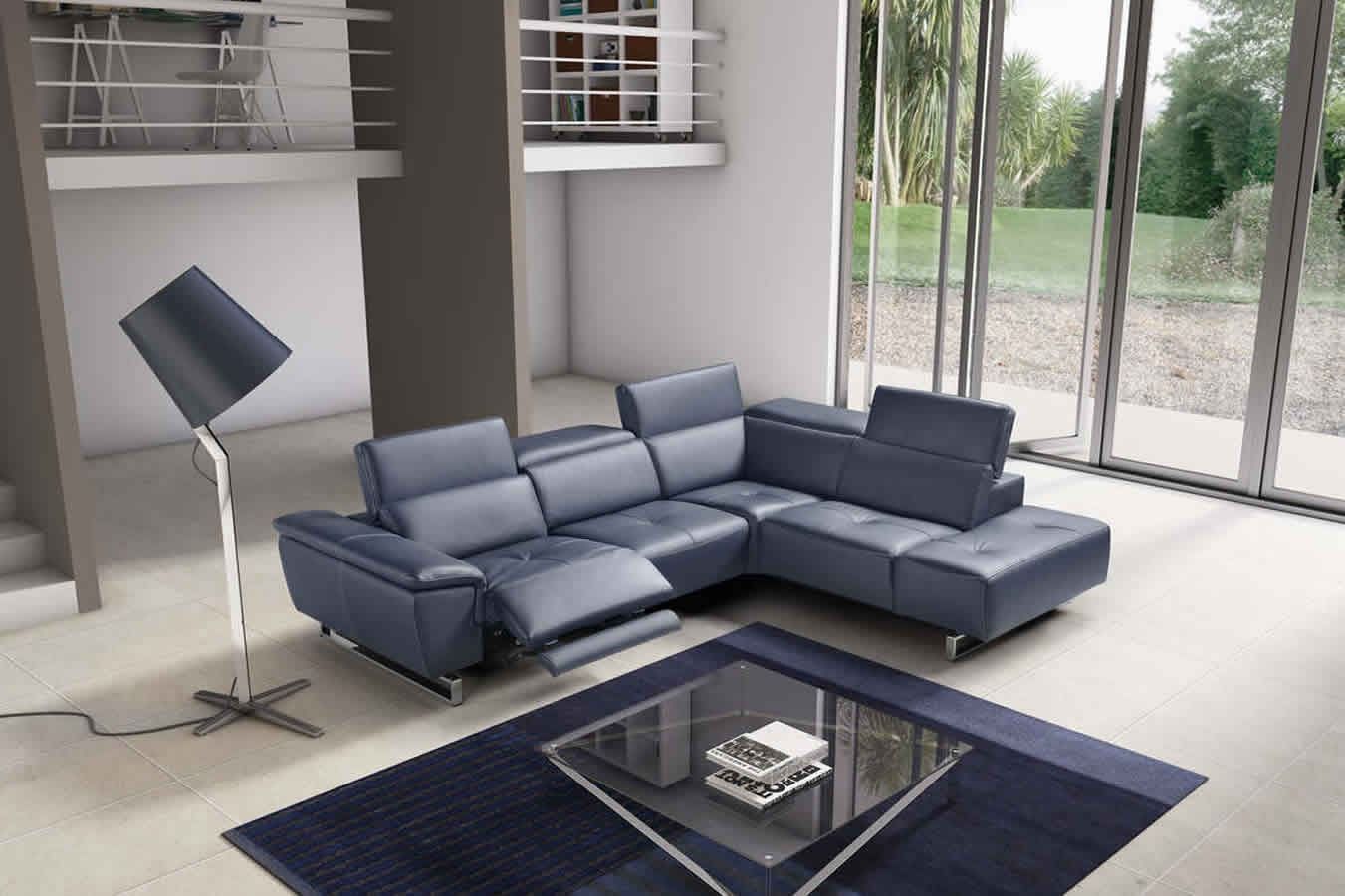 Divano componibile moderno blu in un soggiorno, posizionato vicino a una grande finestra, tappeto scuro e una lampada.