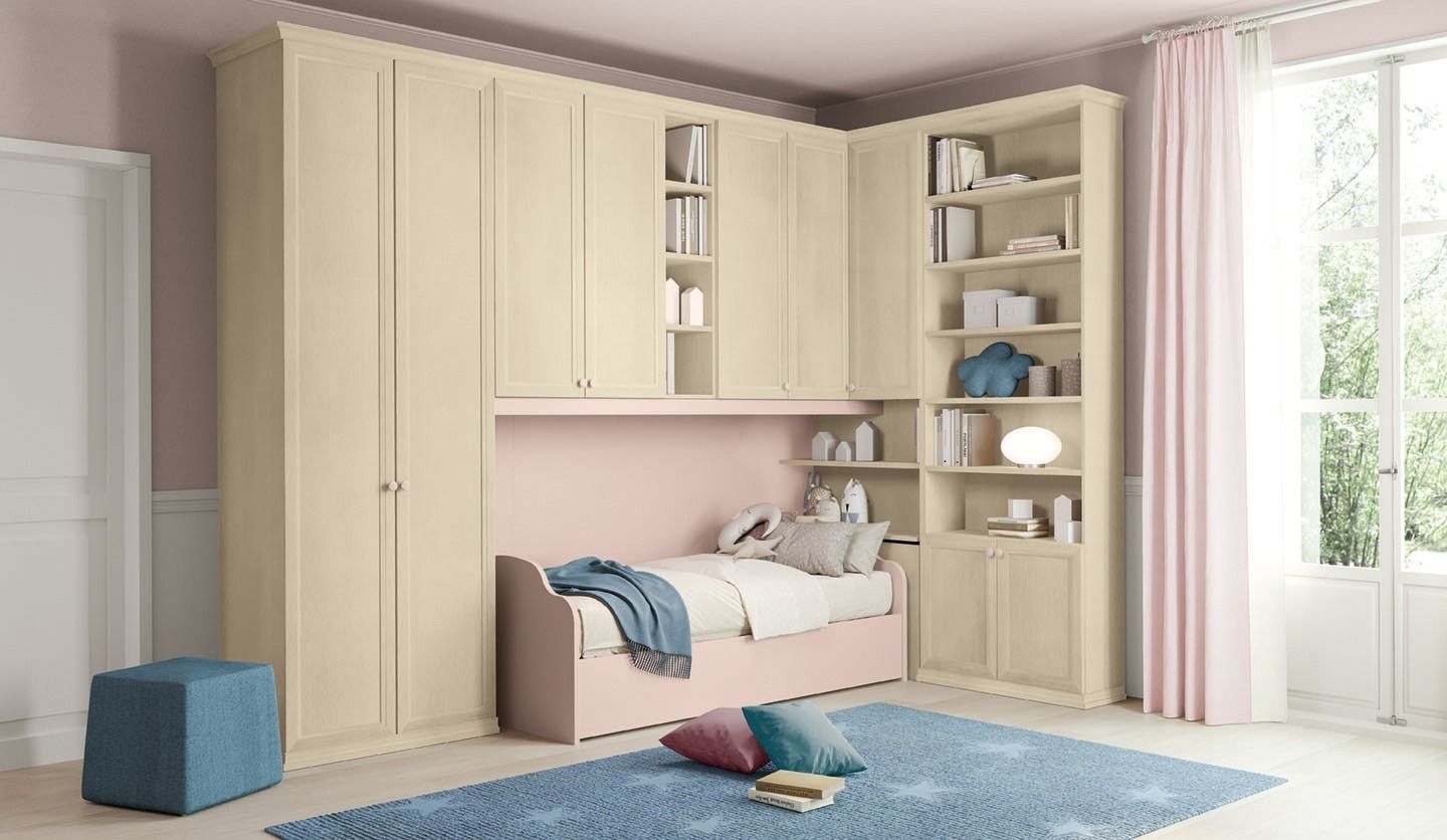 Una camera da letto con armadi a muro color crema, un letto rosa e una libreria. Un tappeto blu e una finestra con tende rosa.