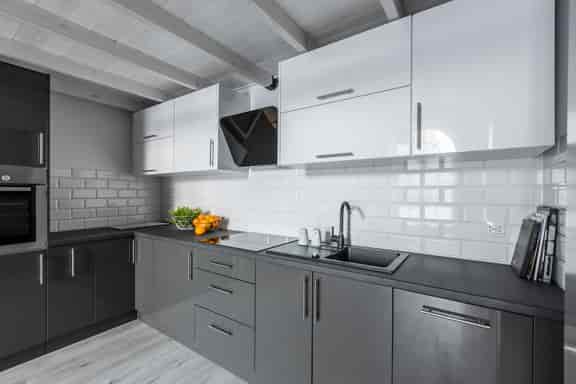 This is a kitchen with grey base units and white wall units and the splash back is white gloss brick tiles