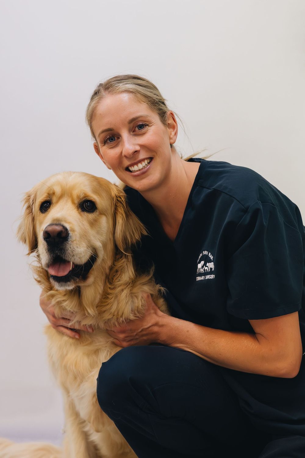 A woman in scrubs is kneeling down next to a dog.