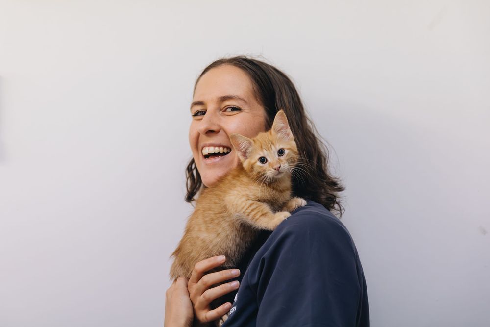 A woman is holding an orange kitten on her shoulder.