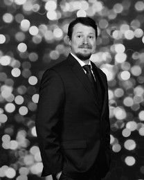 Man in suit, hands in pockets, posing in front of blurred lights.