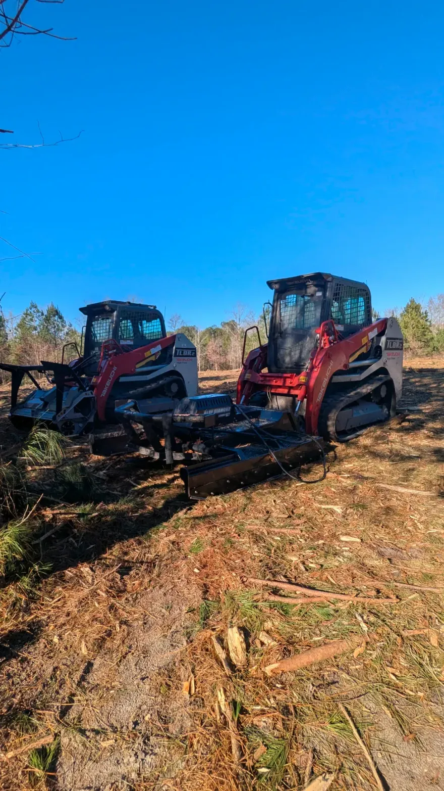 Two red harvesters parked in a cleared field under a bright blue sky