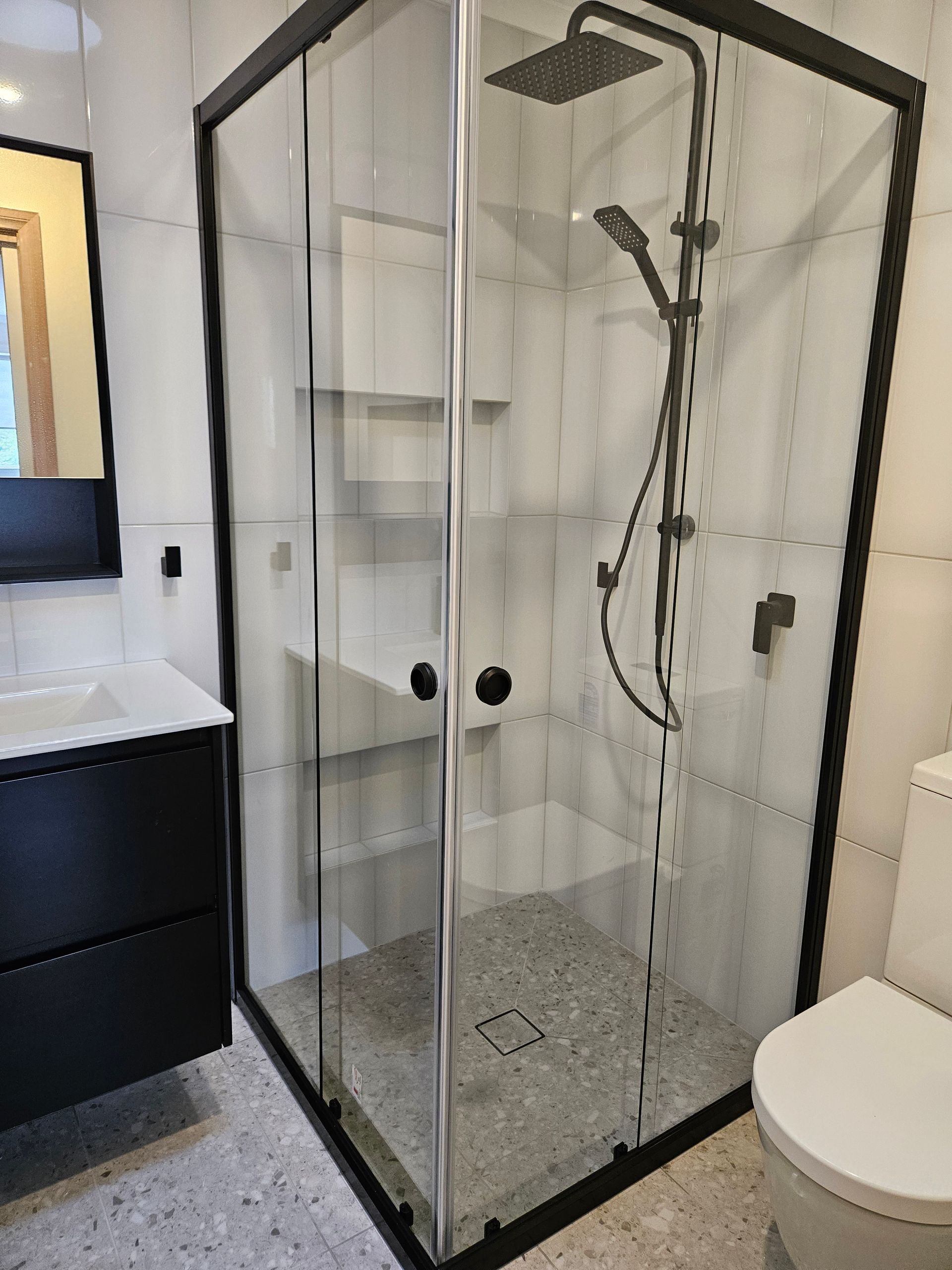 A bathroom with a shower , toilet , sink and mirror.