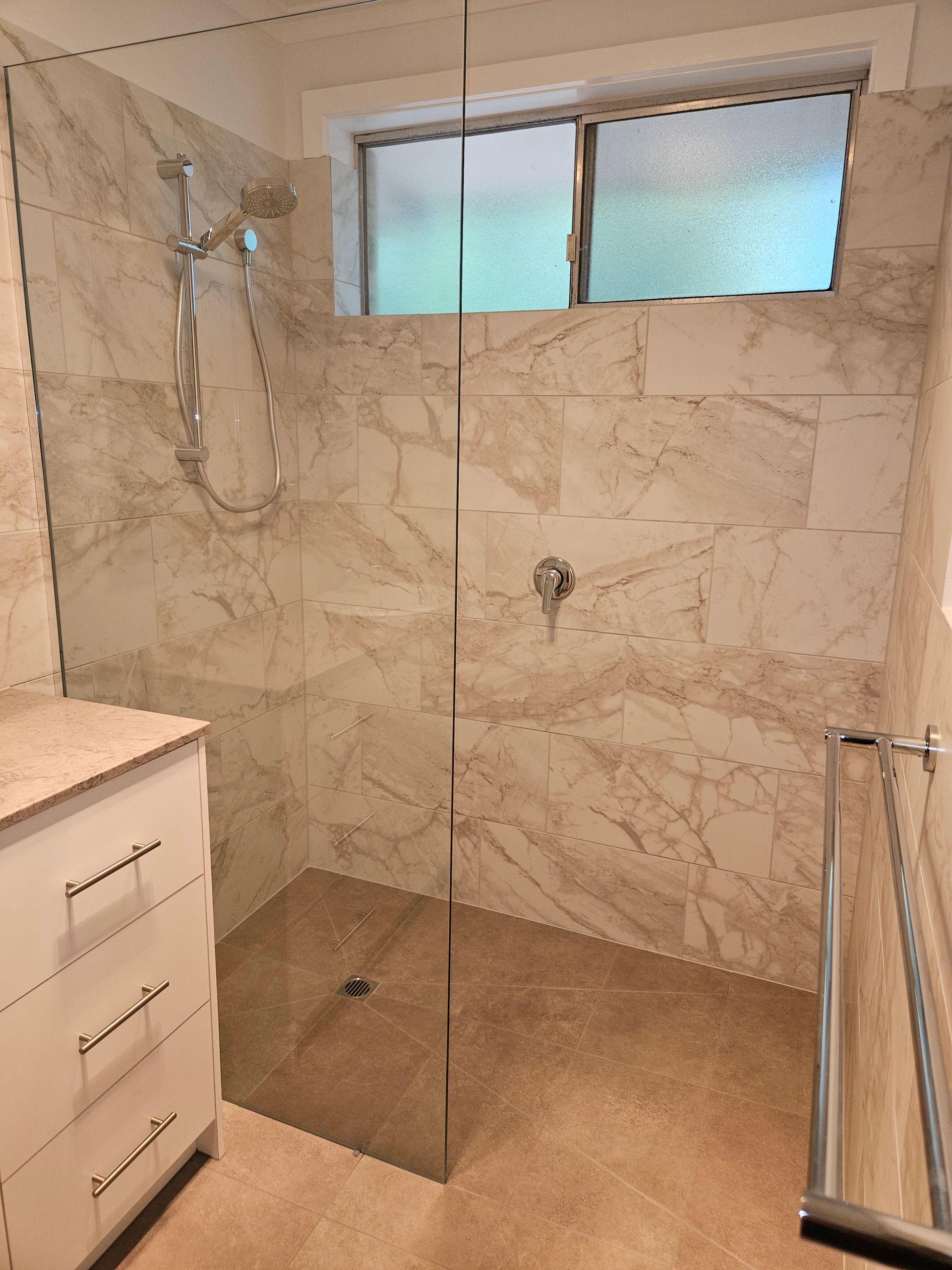 A bathroom with a walk in shower and a window.