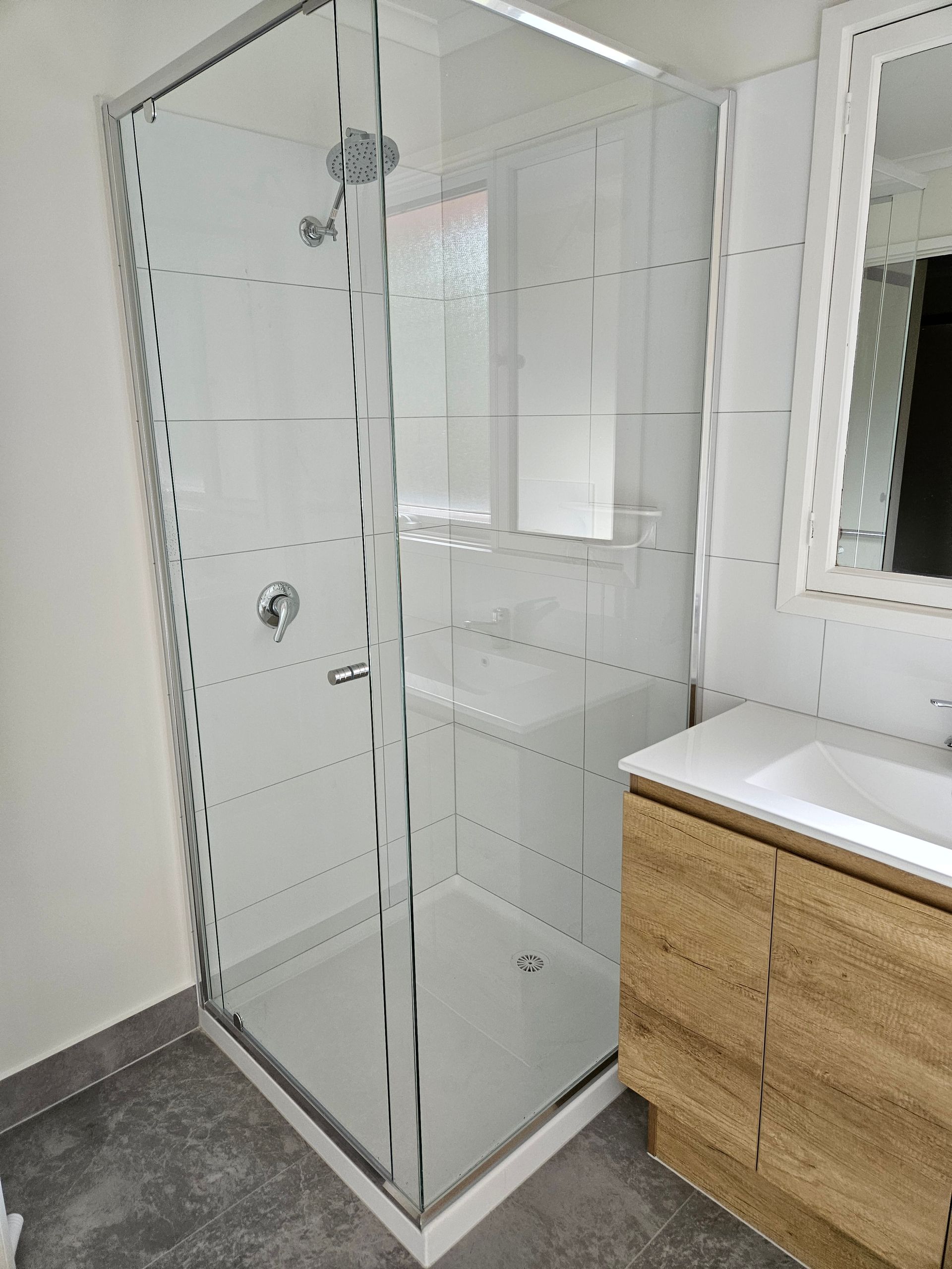 A bathroom with a walk in shower , sink and mirror.