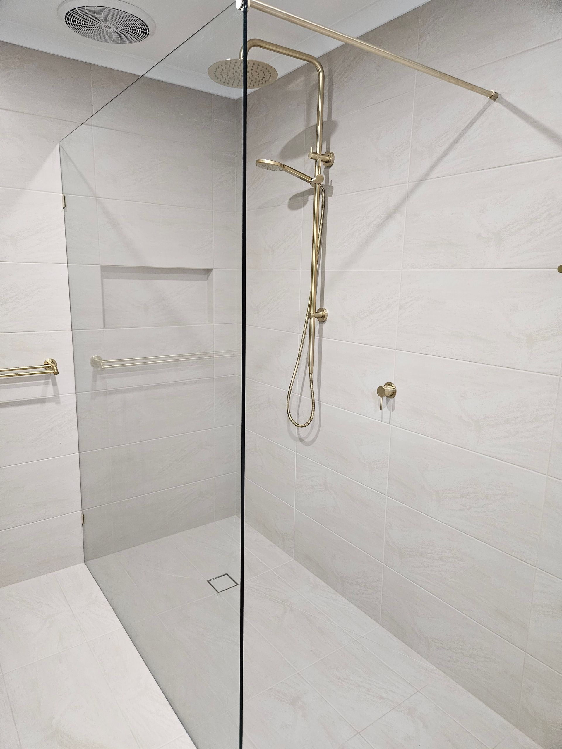 A walk in shower with a glass door and a gold shower head.