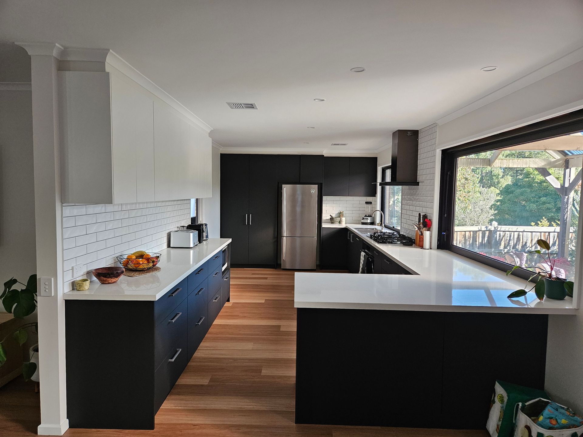 A kitchen with black cabinets and white counter tops and a large window.