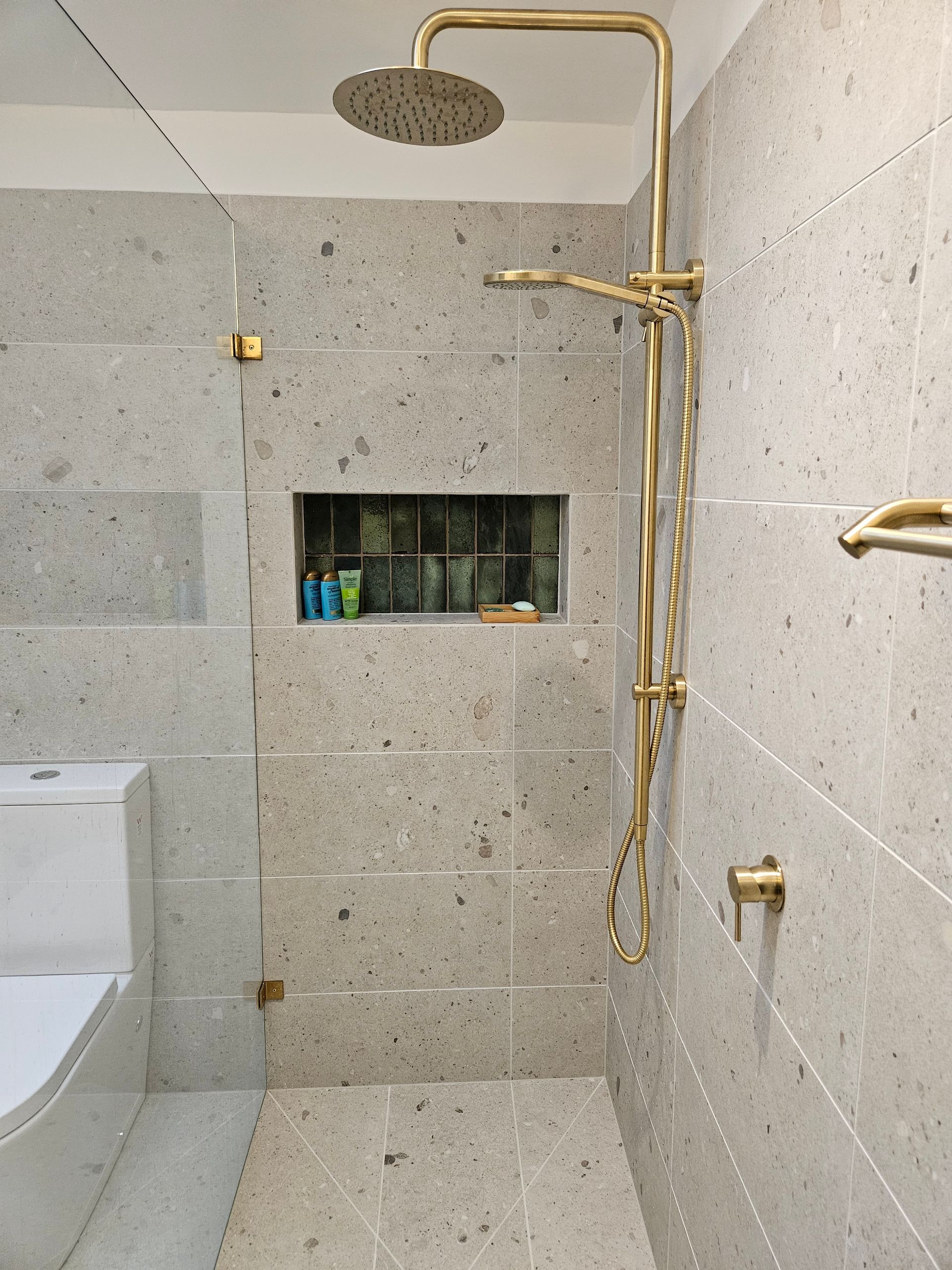 A bathroom with a walk in shower with a brass shower head