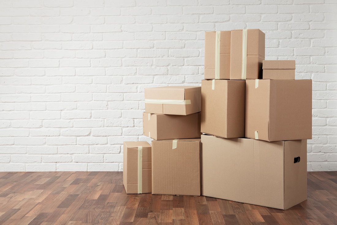 Pile of cardboard moving boxes on a hardwood floor, against a white brick wall.