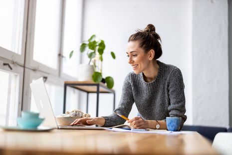 Een vrouw zit aan een tafel en gebruikt een laptop.
