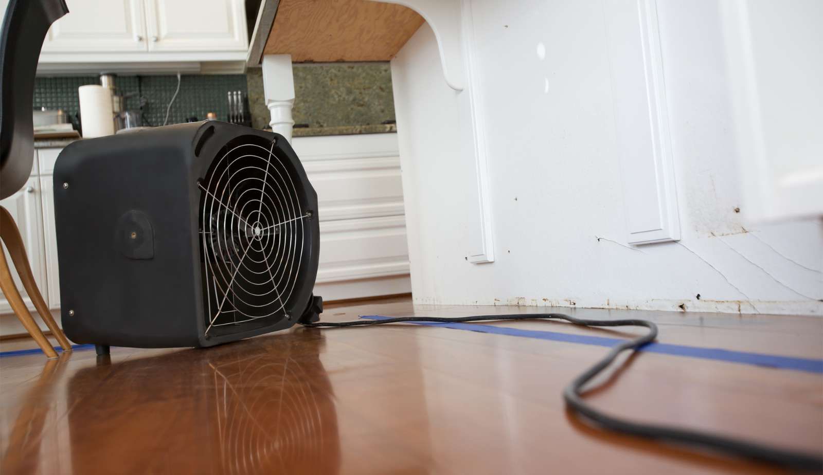 A fan is sitting on a wooden floor in a kitchen.