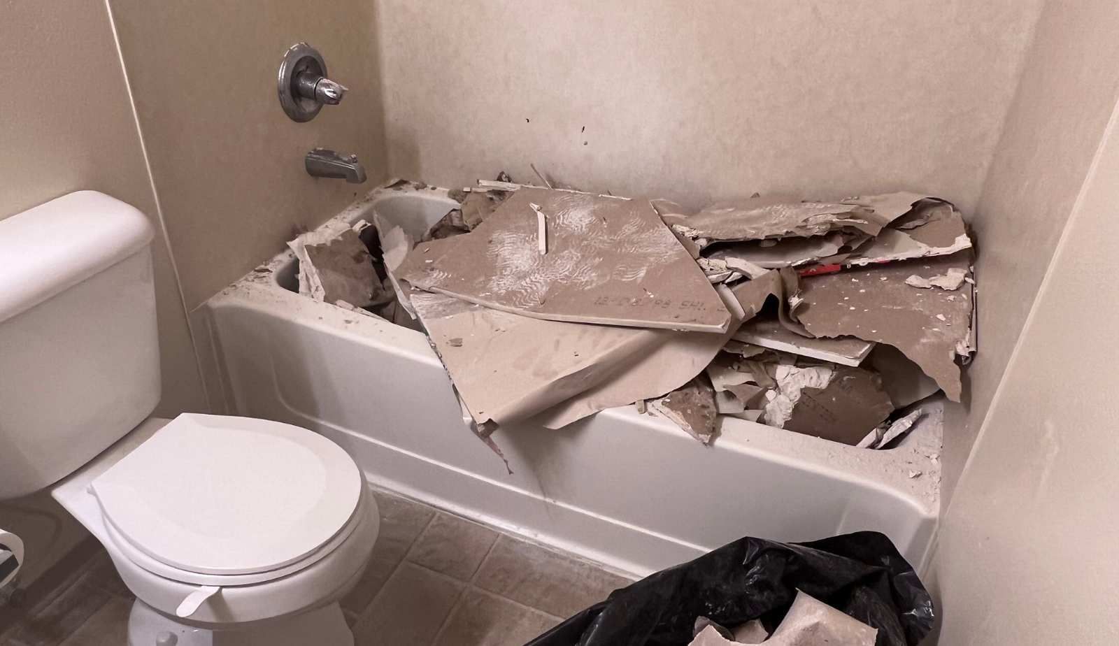 A bathroom with a toilet , bathtub and trash can with severe water damage in Louisiana