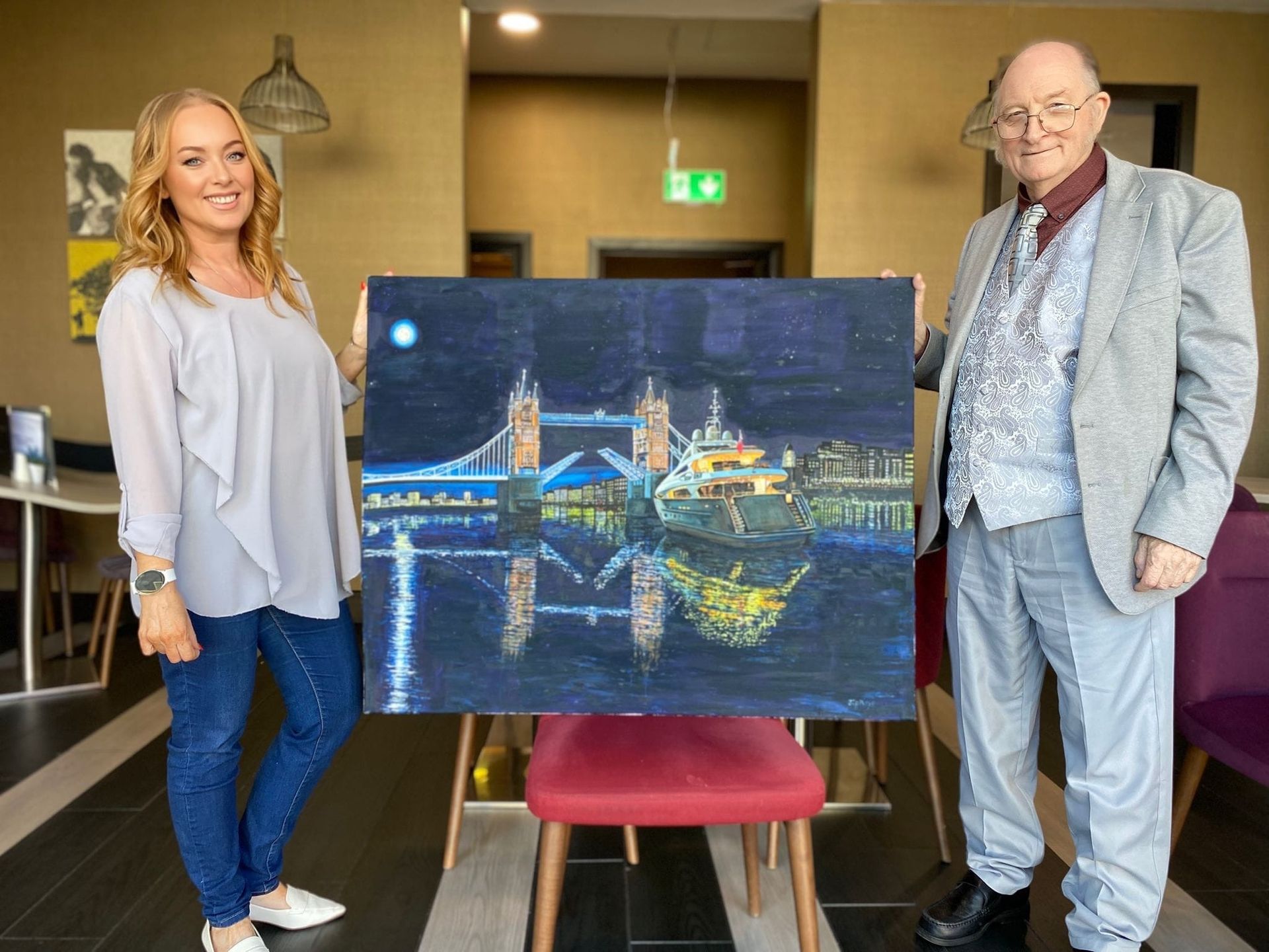 Renowned Welsh Artist Jeffrey Phillips and International Agent Donna Phillips stand with a painting of a Superyacht at Tower Bridge, London.