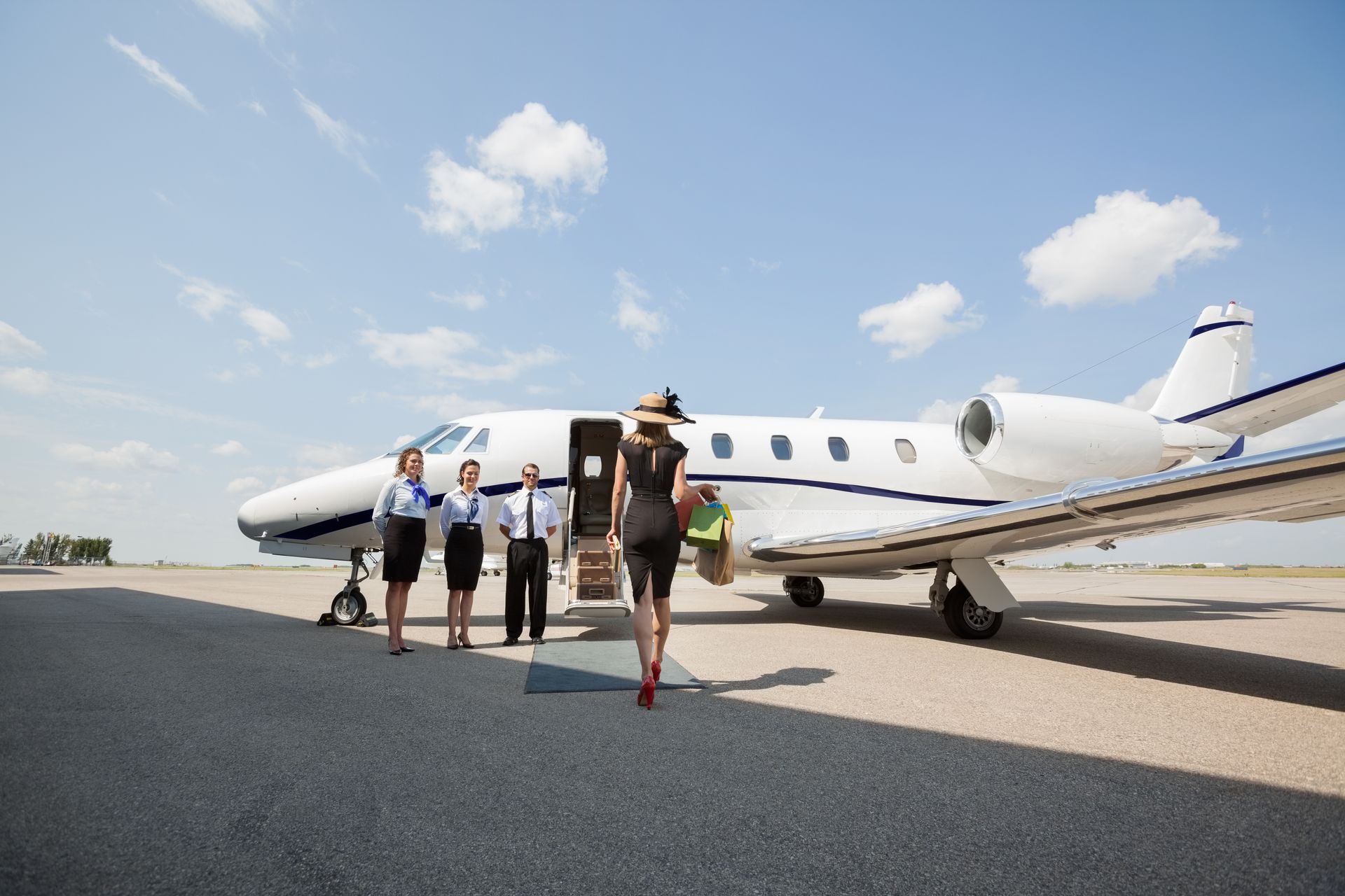 Woman boarding private jet; crew waiting, sunny day.