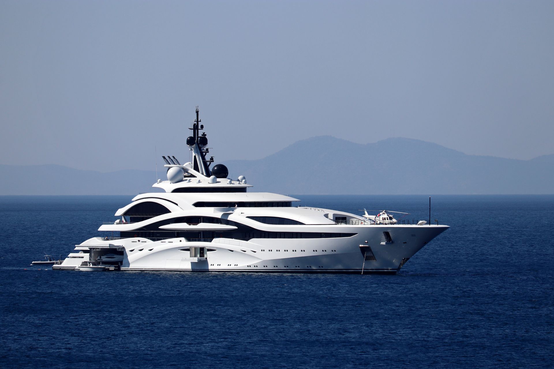 large modern white megayacht with helicopter on forward deck sails the Aegeon