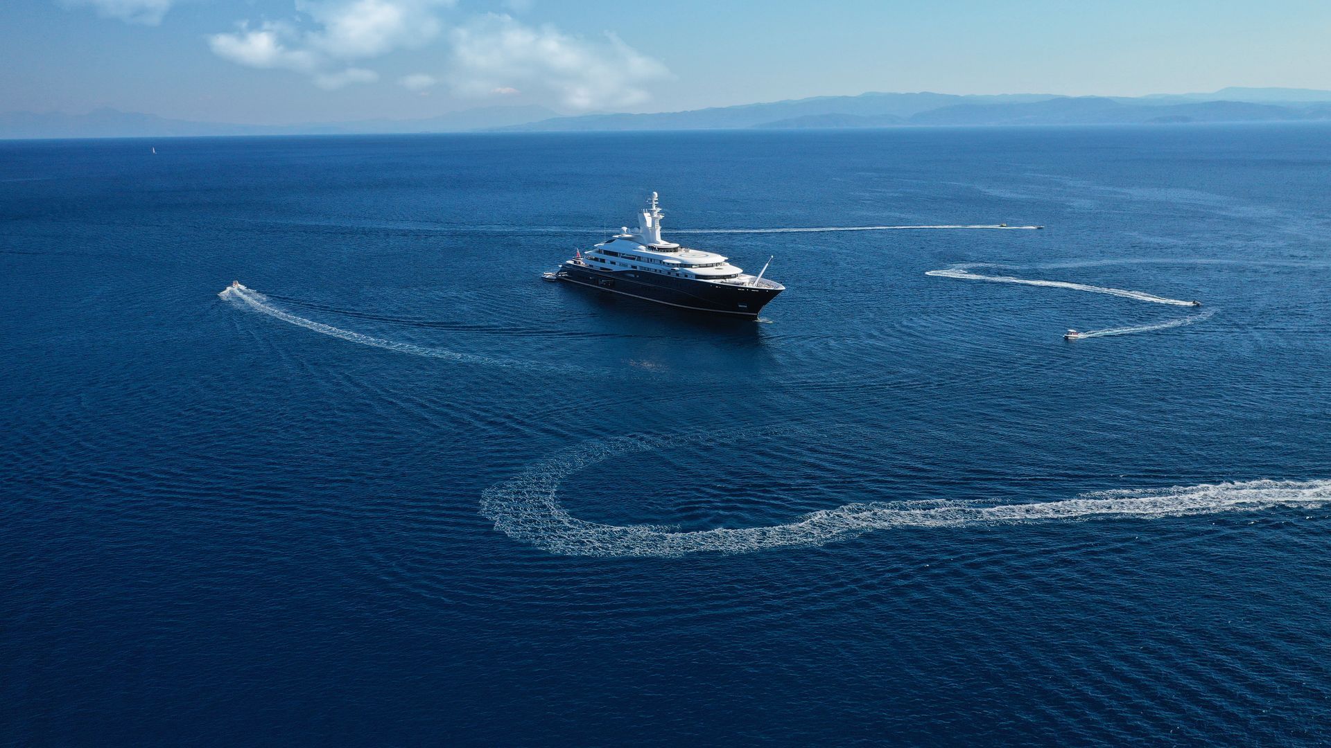 Superyacht in calm sea being circled by jetskis and tender