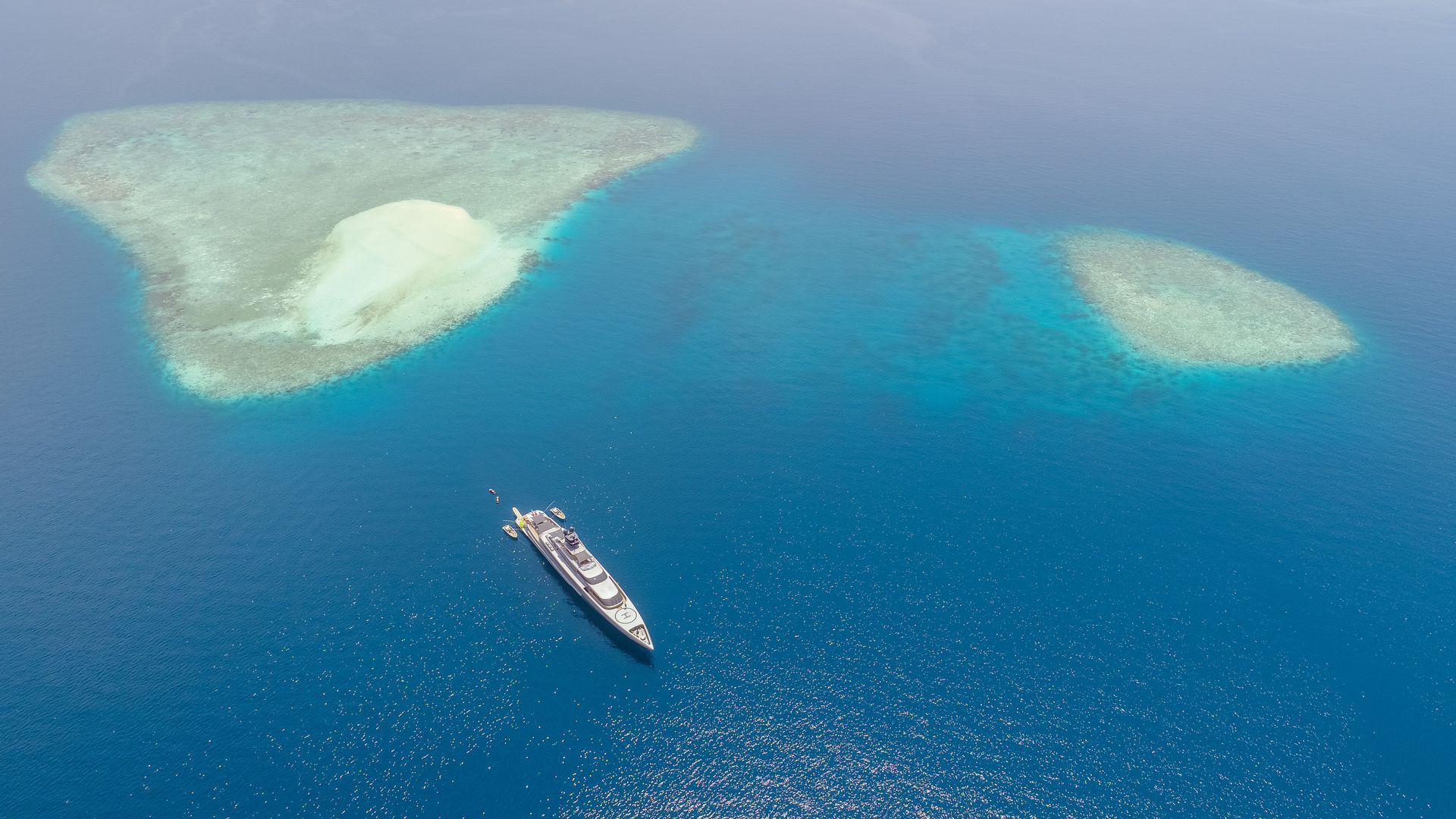 Superyacht moored off tropical island with tenders berthed alongside beach club