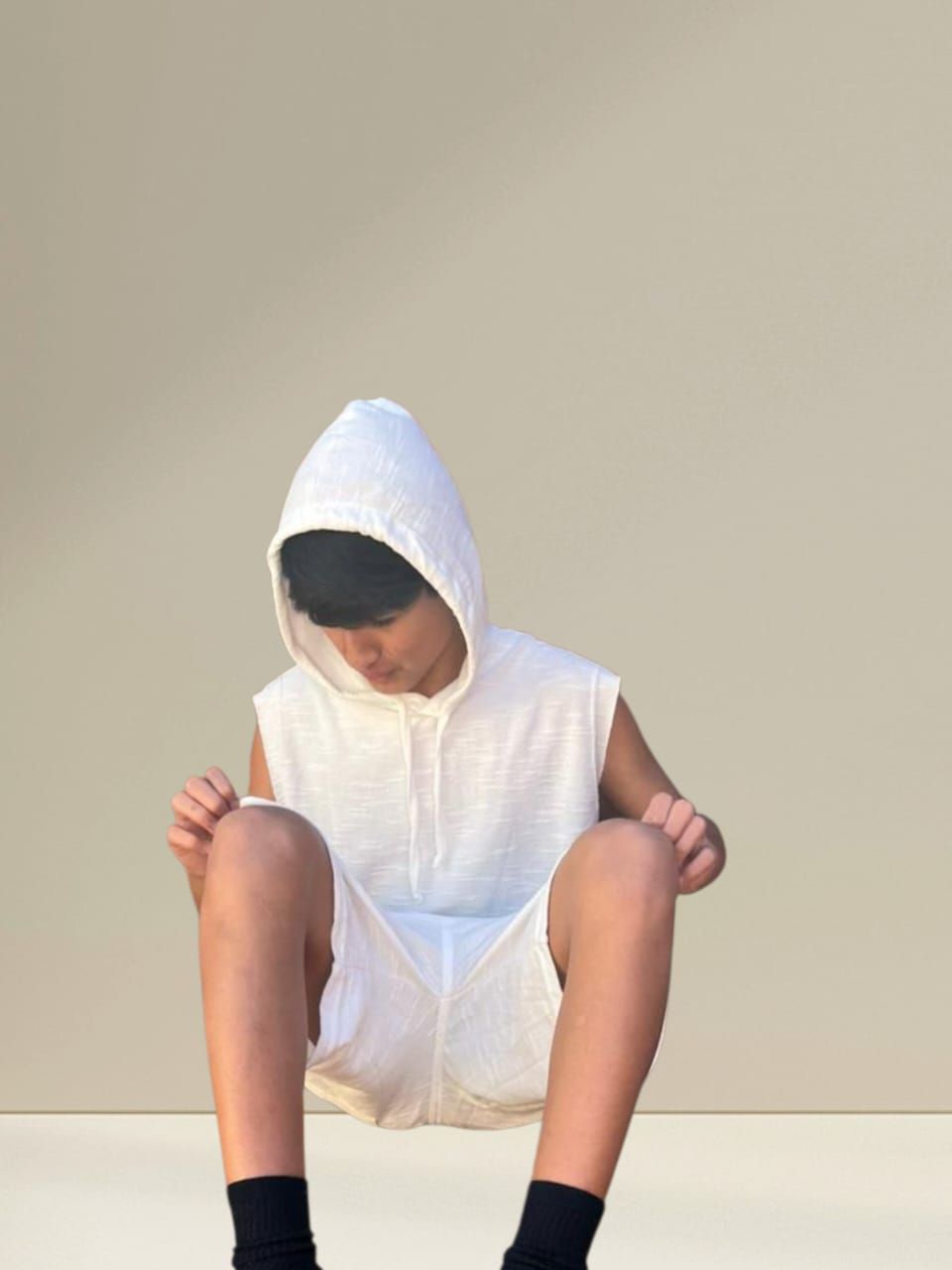 Persona vestida con un chaleco blanco con capucha y pantalones cortos, sentada y mirando hacia abajo.