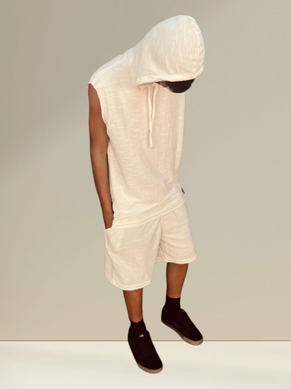 Persona vestida con un chaleco blanco con capucha y pantalones cortos, sentada y mirando hacia abajo.