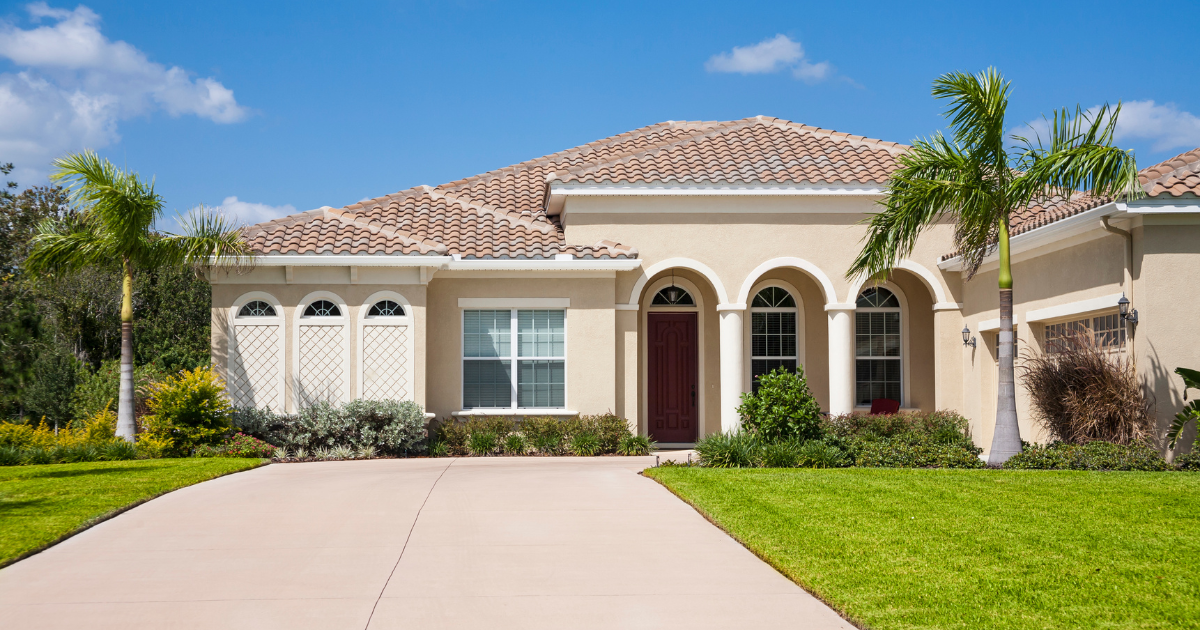 Single-story stucco house with a tile roof, arched entry, and a driveway in front