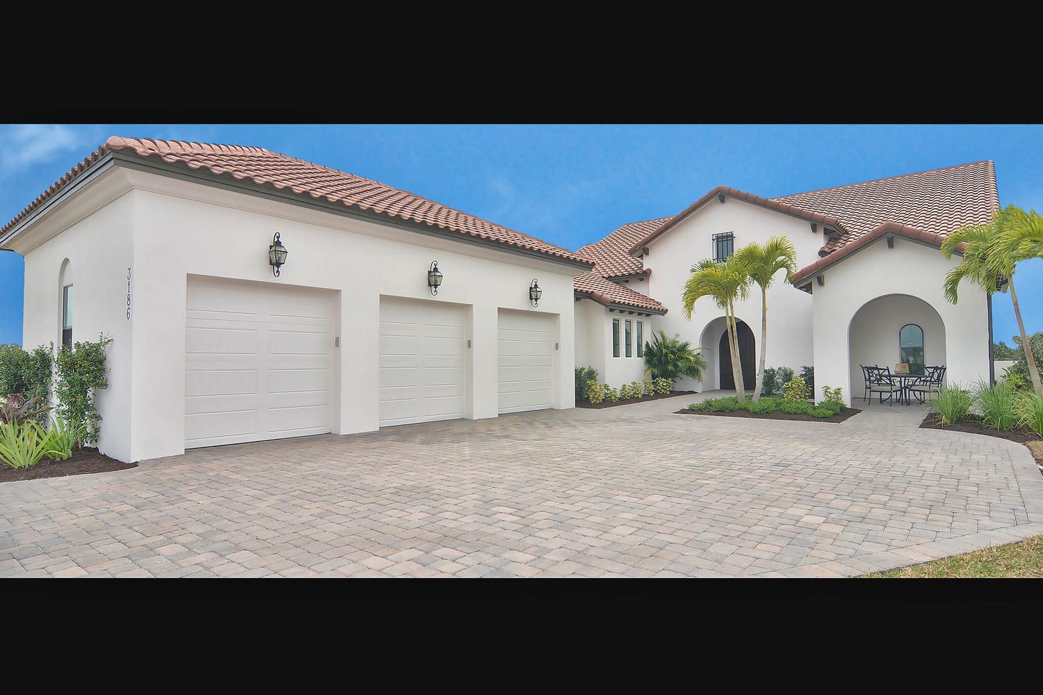 Luxury white stucco house with red tile roof, three-car garage, and palm trees on a cobblestone driveway