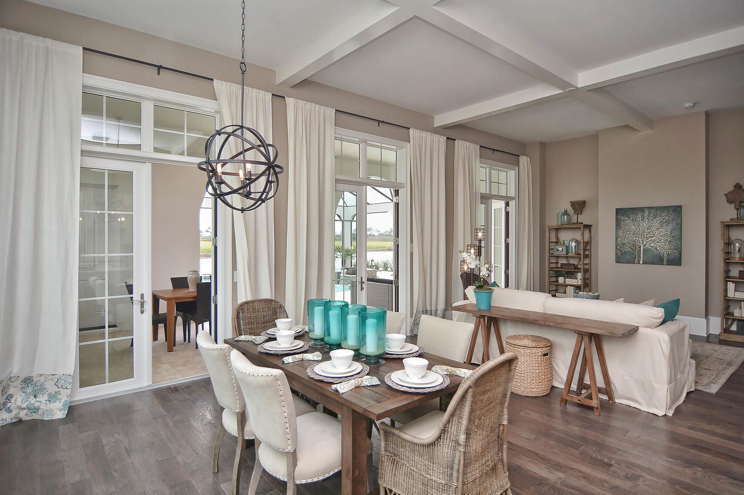 Elegant dining room with glass table, wicker chairs, beige sofa, and tall curtains by bright windows