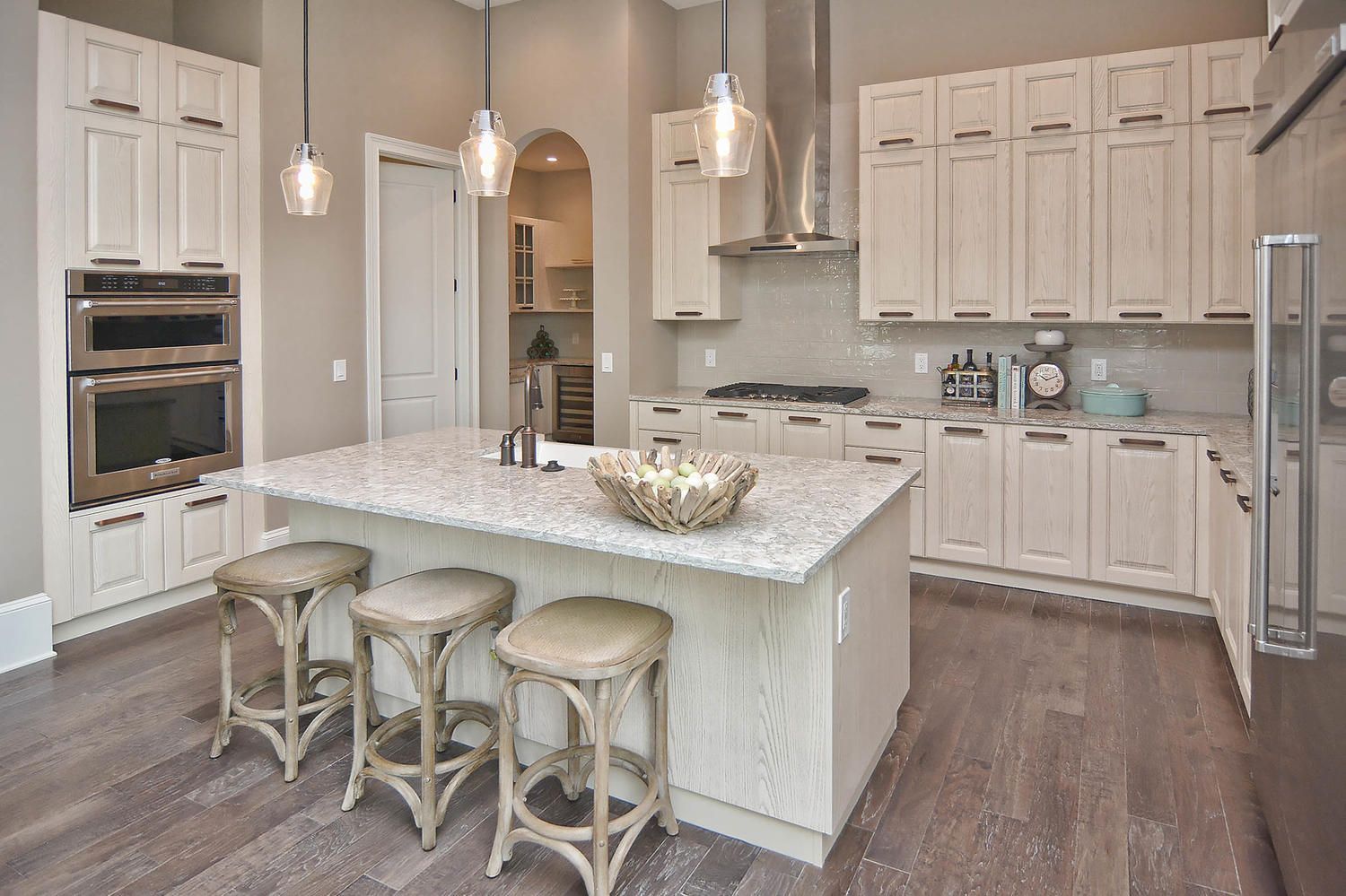Bright modern kitchen with white cabinets, granite island, pendant lights, and three stools