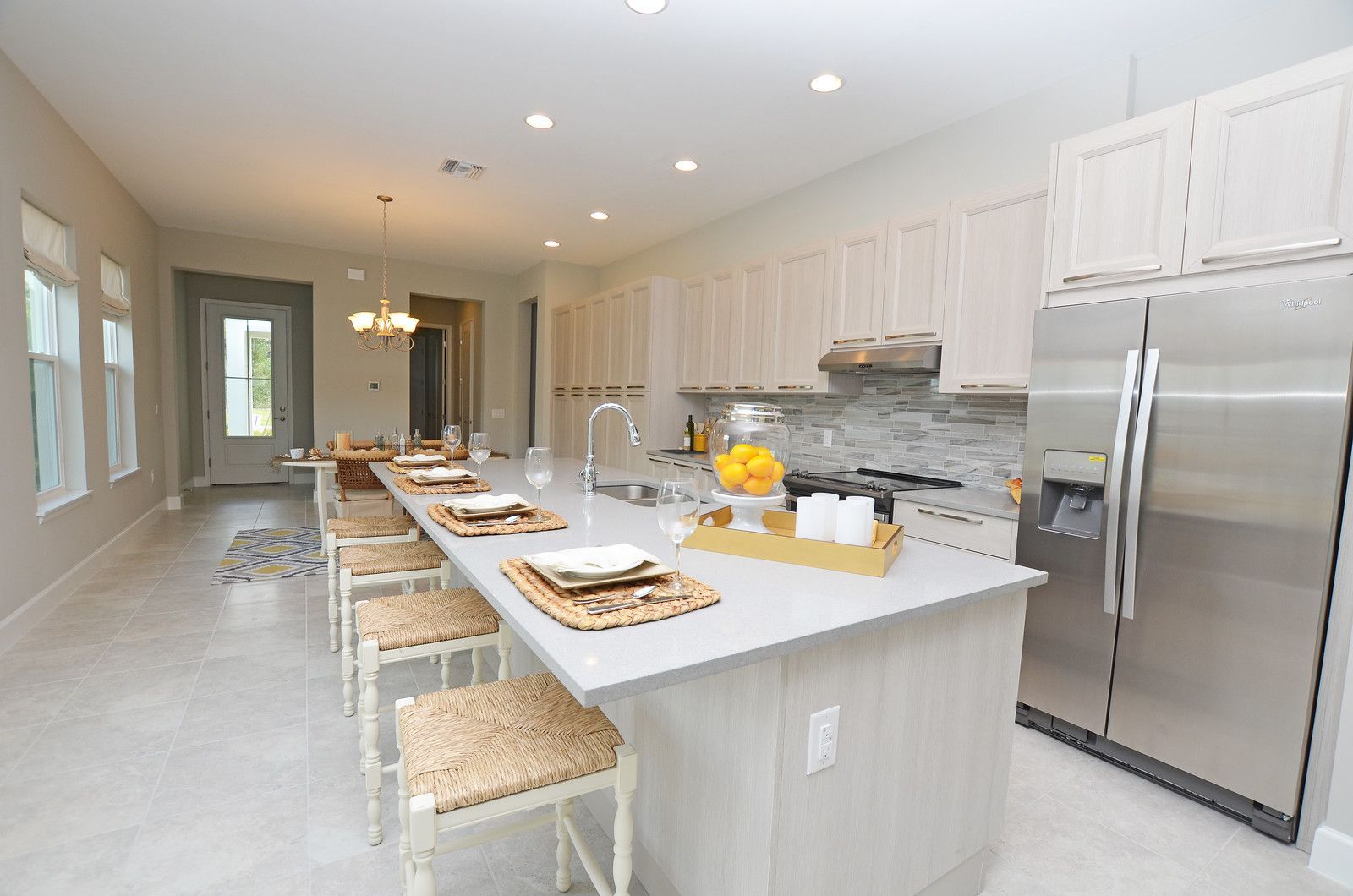 Bright modern kitchen with white cabinets, island seating, stainless steel fridge, and set dining table