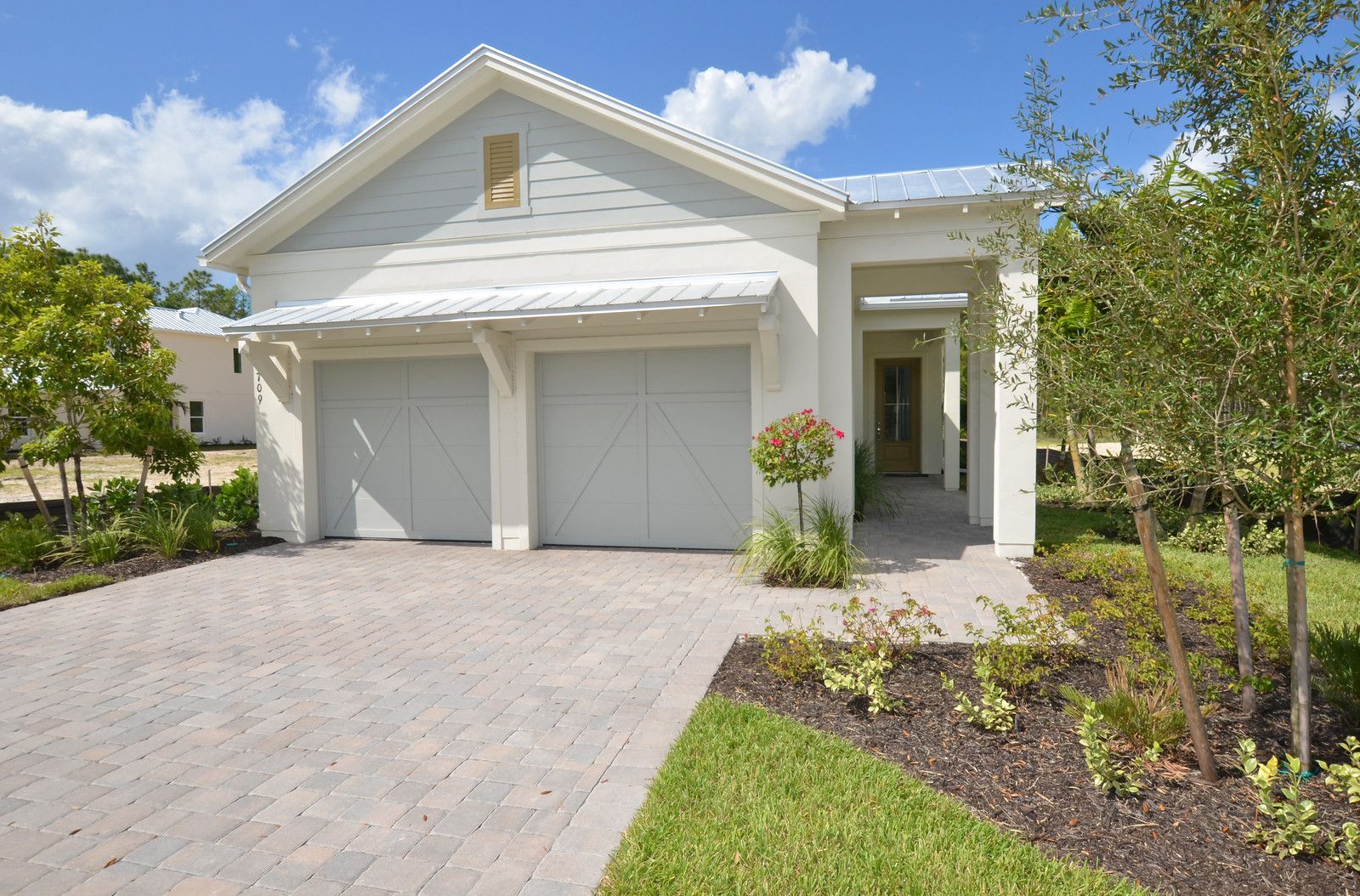 Single-story white house with a double garage, paved driveway, and landscaped front yard under a blue sky