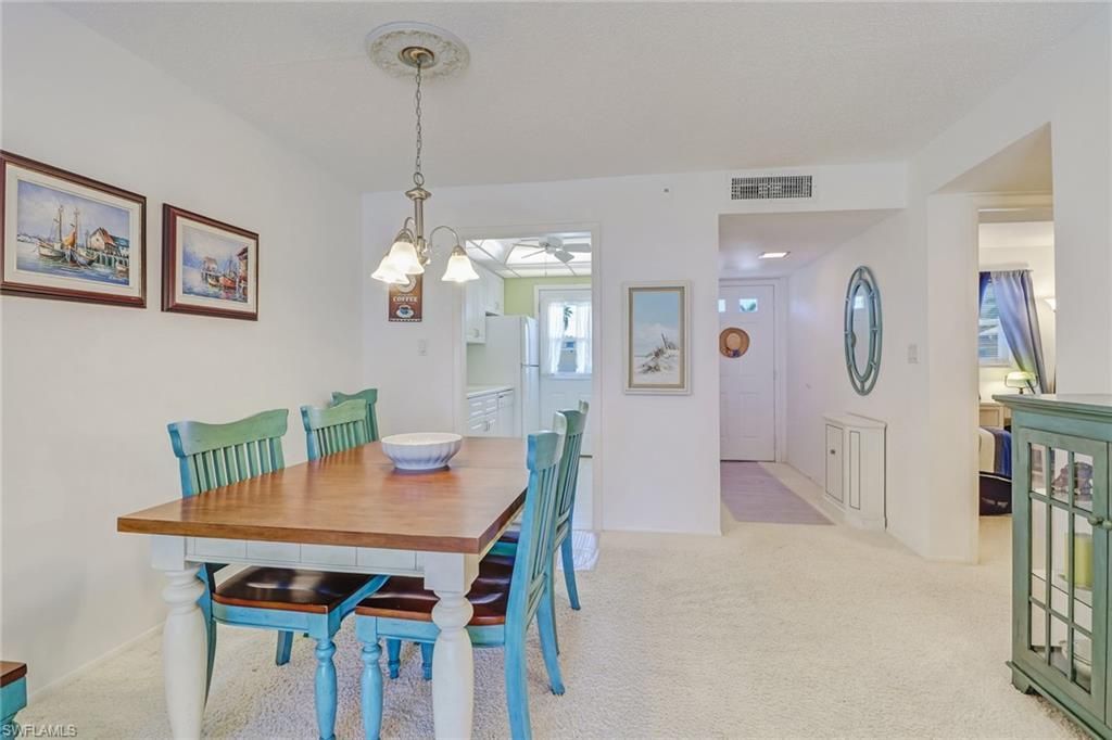 Bright dining room with a wooden table, teal chairs, hanging light, and open view into a kitchen.