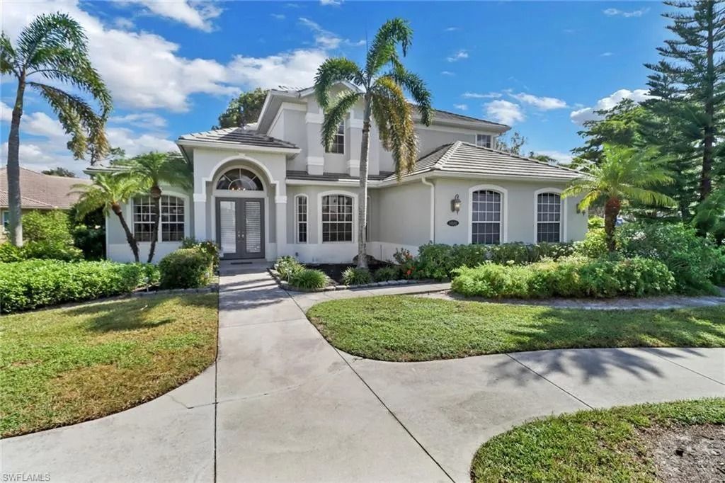 Large white suburban house with arched entry, palm trees, and a curved driveway under a blue sky