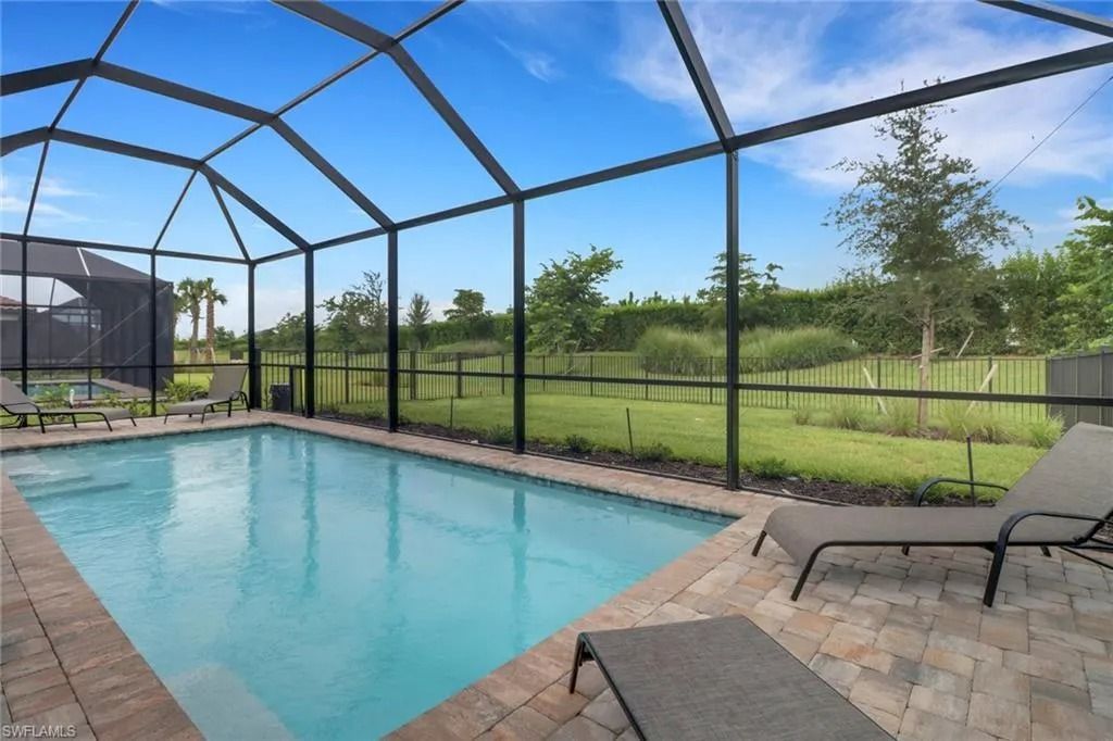 Screened-in backyard pool with lounge chairs and a brick patio beside a grassy yard and trees.