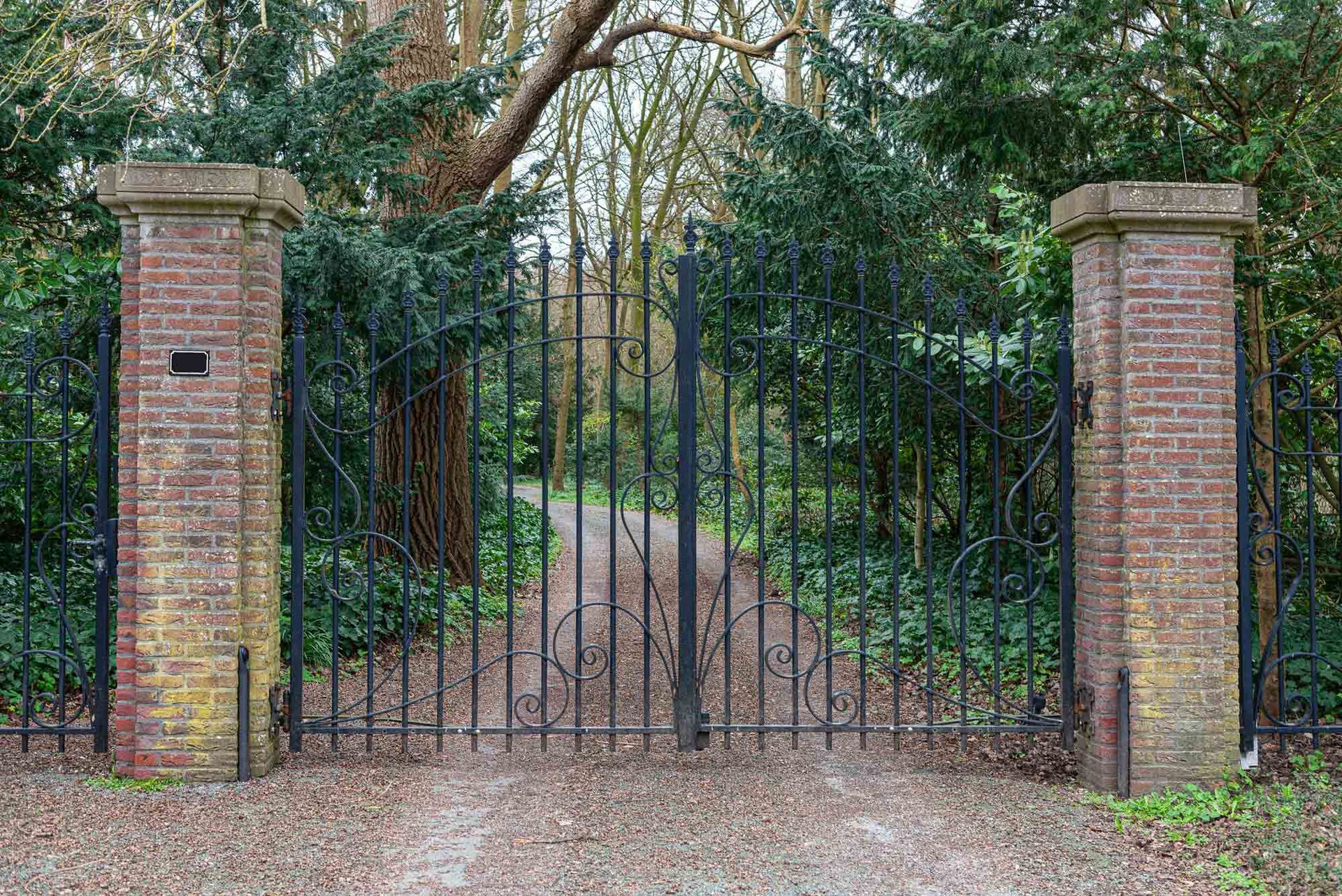 A Wrought Iron Gate Is Surrounded by Brick Pillars and Trees | Cranbourne, VIC | Cranbourne Fencing Pty Ltd
