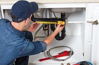 A plumber is measuring a pipe under a sink.