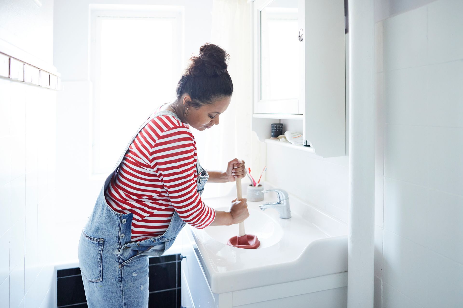 Woman unclogging sink with plunger in bathroom