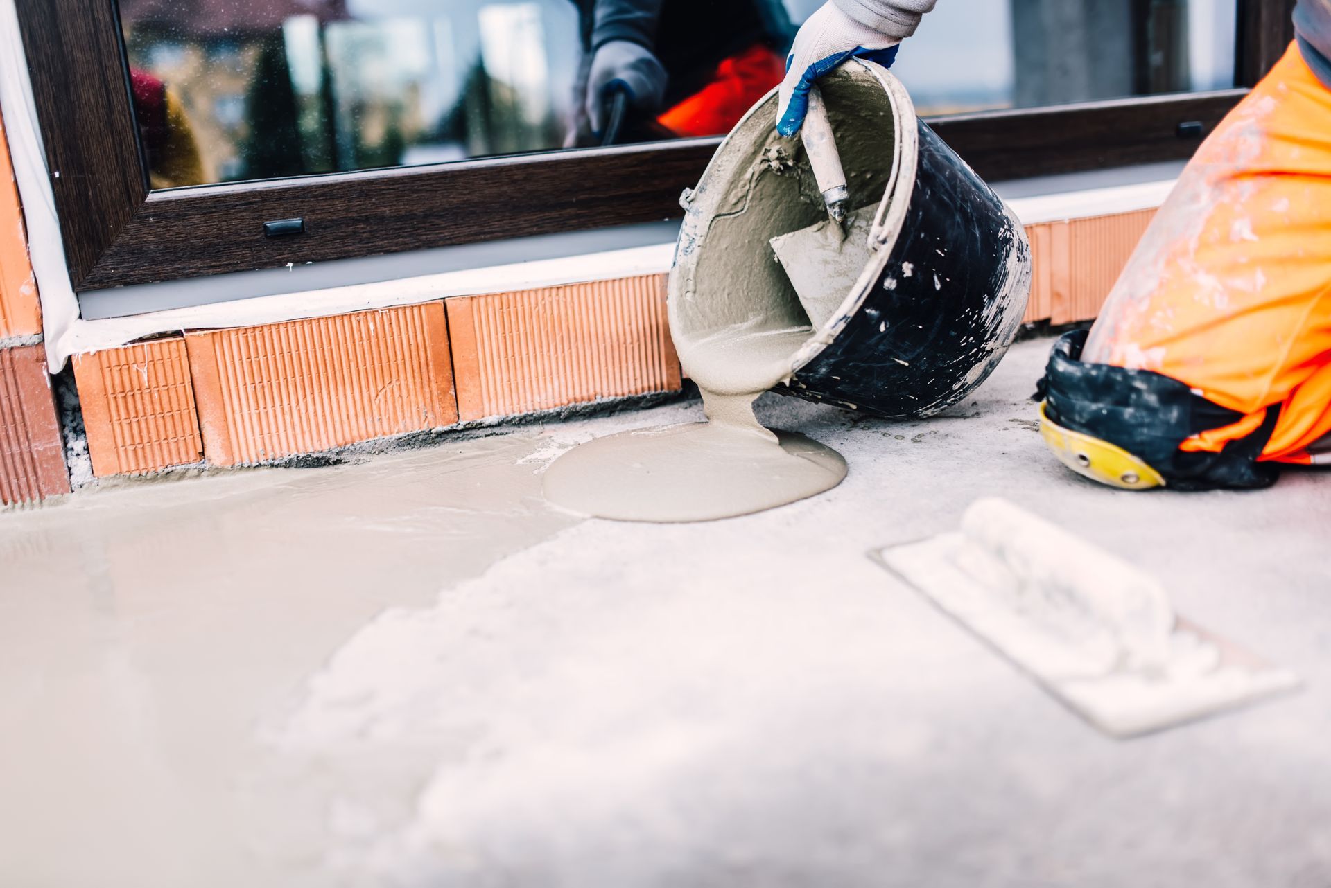 A person is pouring cement into a bucket with a trowel.