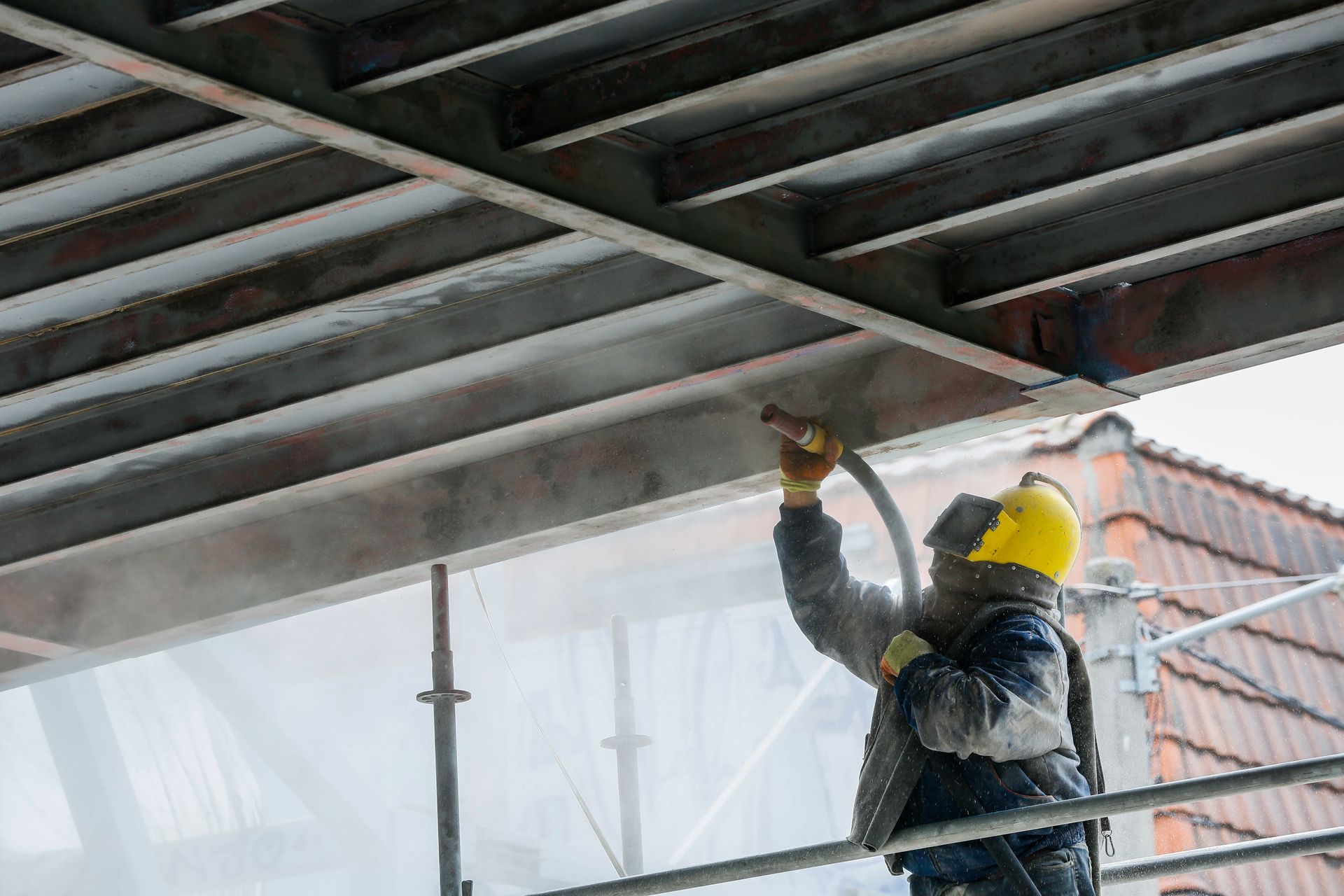 A construction worker is spray painting the ceiling of a building.